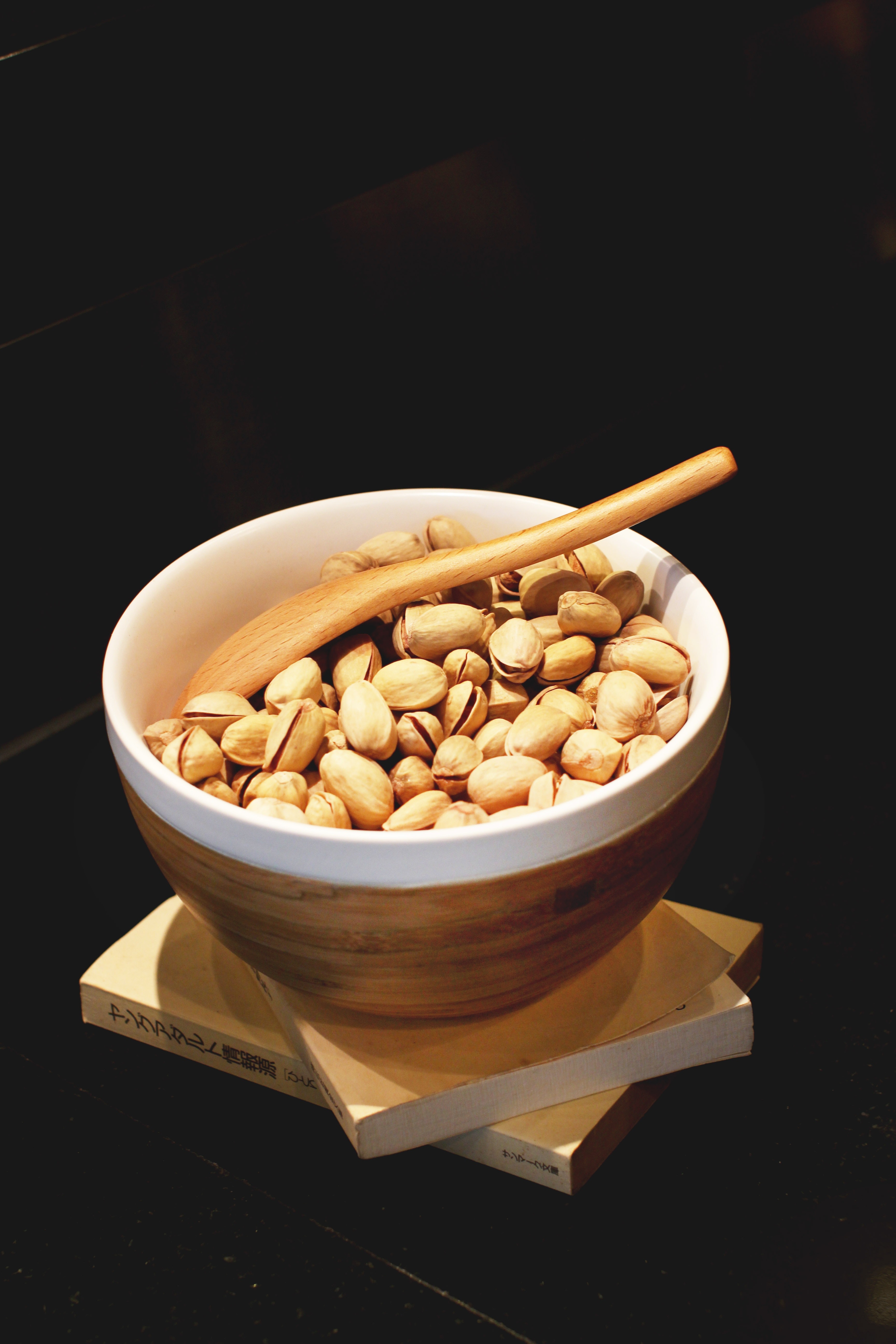 Pistachio nuts in white and brown ceramic bowl with brown wooden spoon photo