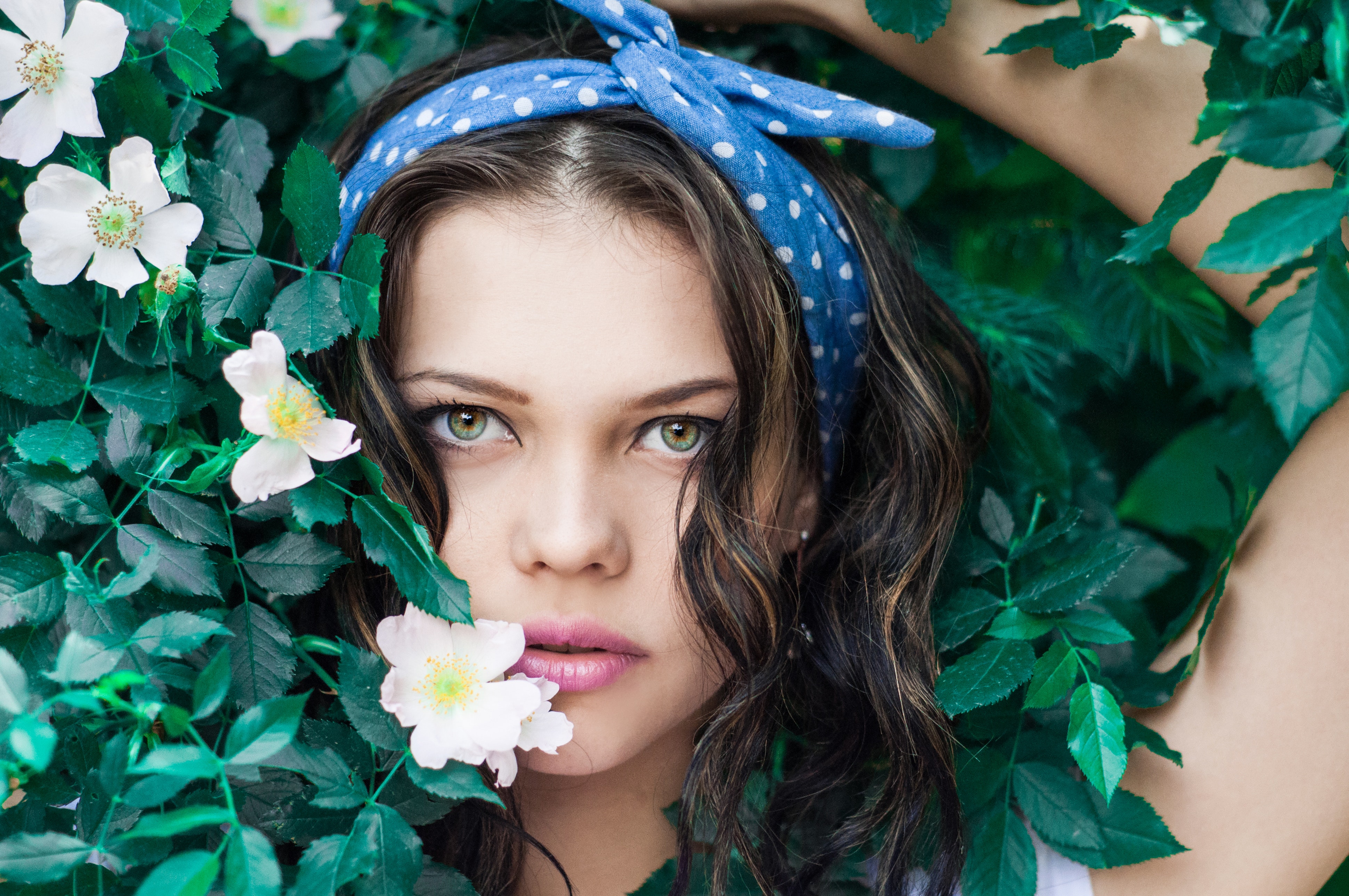 Portrait photo of woman in white top and blue polka dot headband near flowers