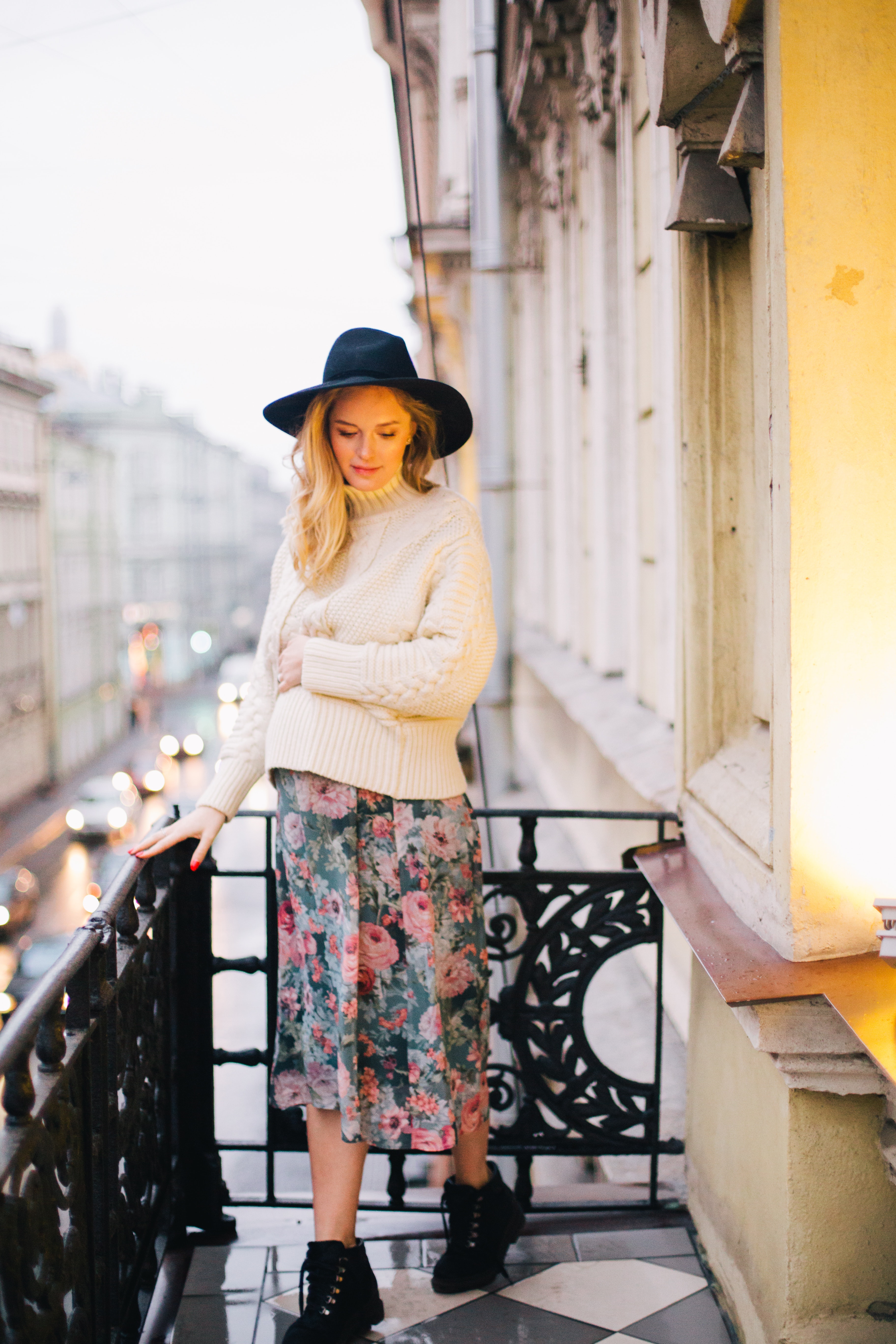 Pregnant woman wearing white sweater and multicolored floral skirt standing on balcony photo