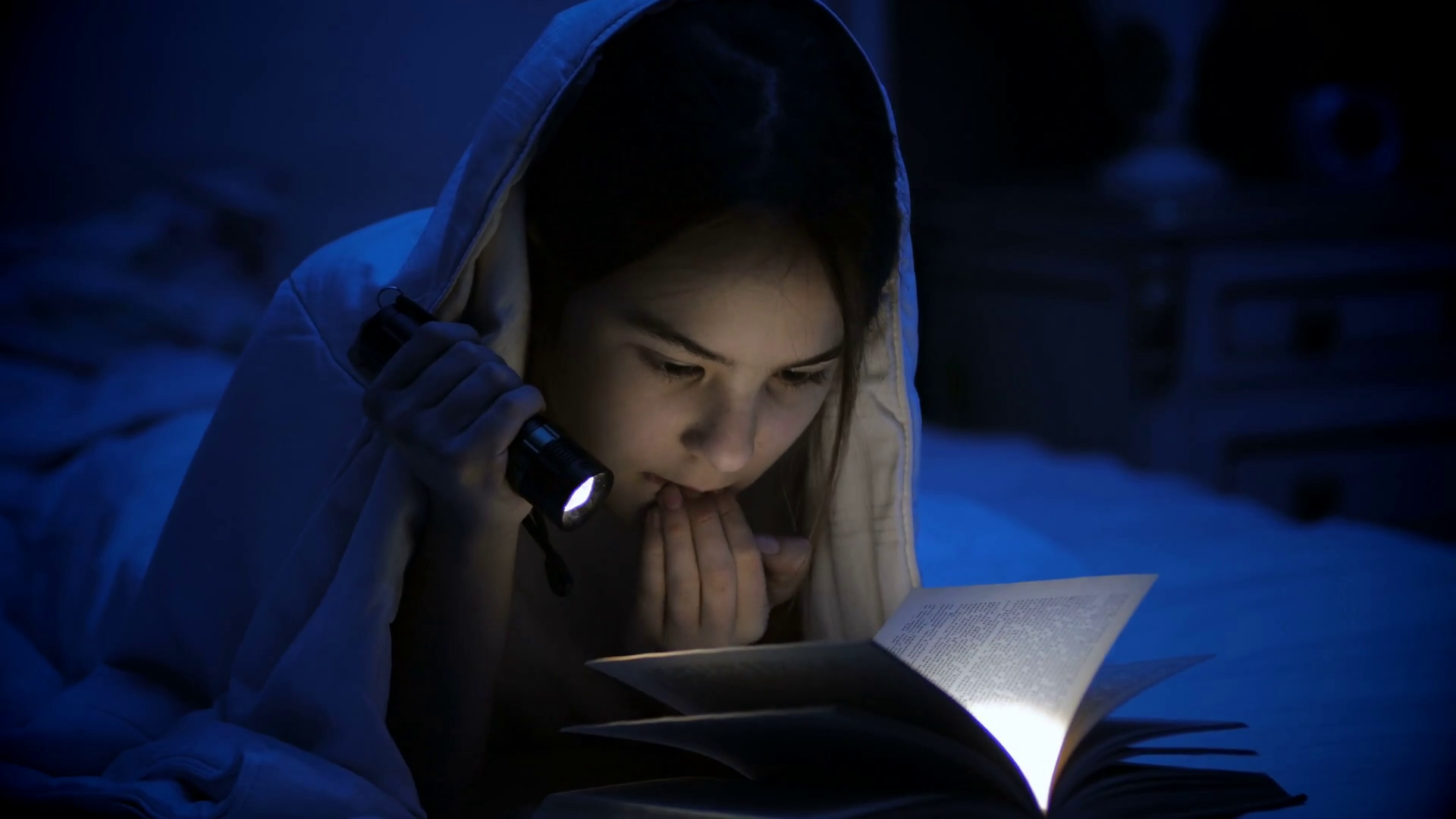 4k video of young girl reading book at night flashlight lying under ...