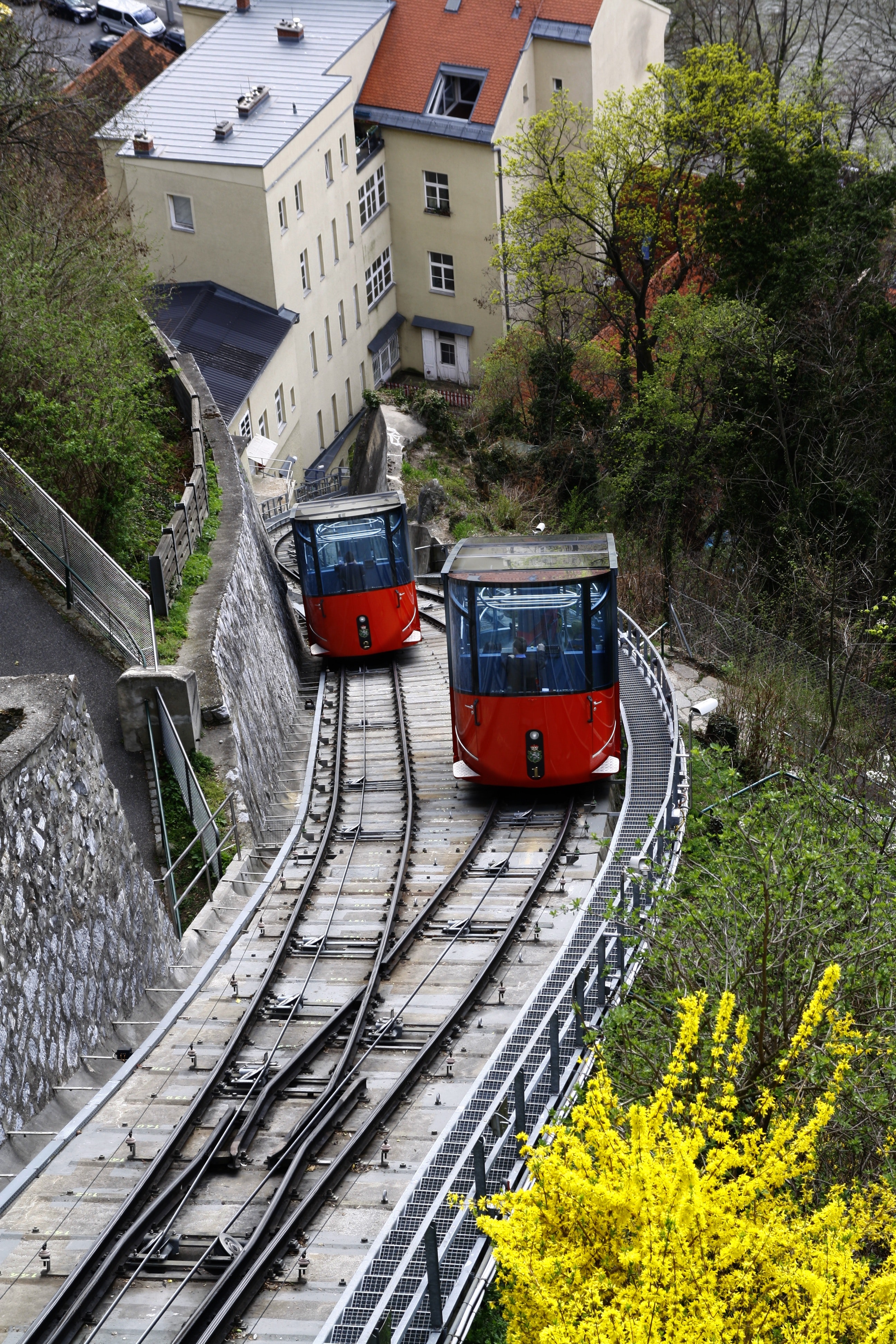 Red and black cable train uphill near the houses during daytime photo