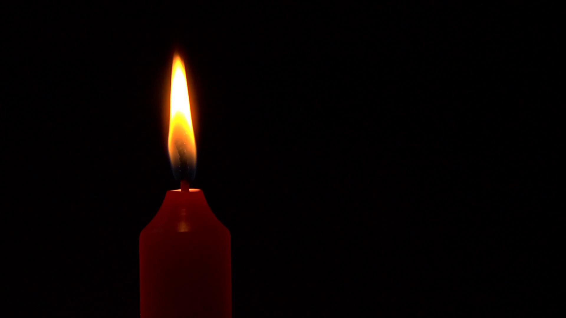 A red candle flame burns in the darkness, slow motion, then is blown ...