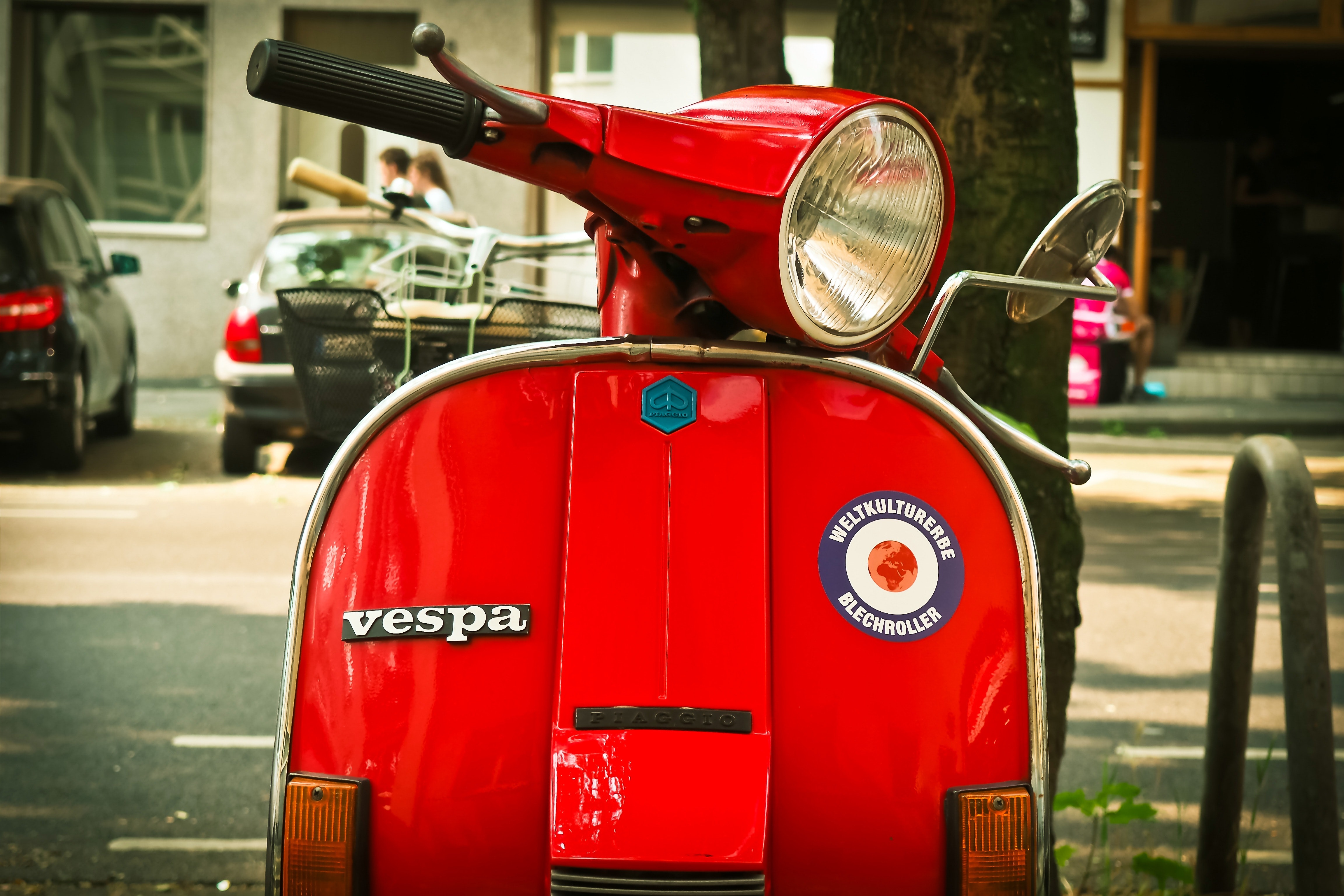 Red vespa motor scooter parked near tree during daytime photo
