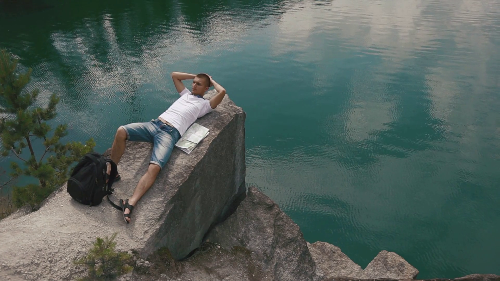 Young tourist man relaxes by resting on rock near calm mountain lake ...