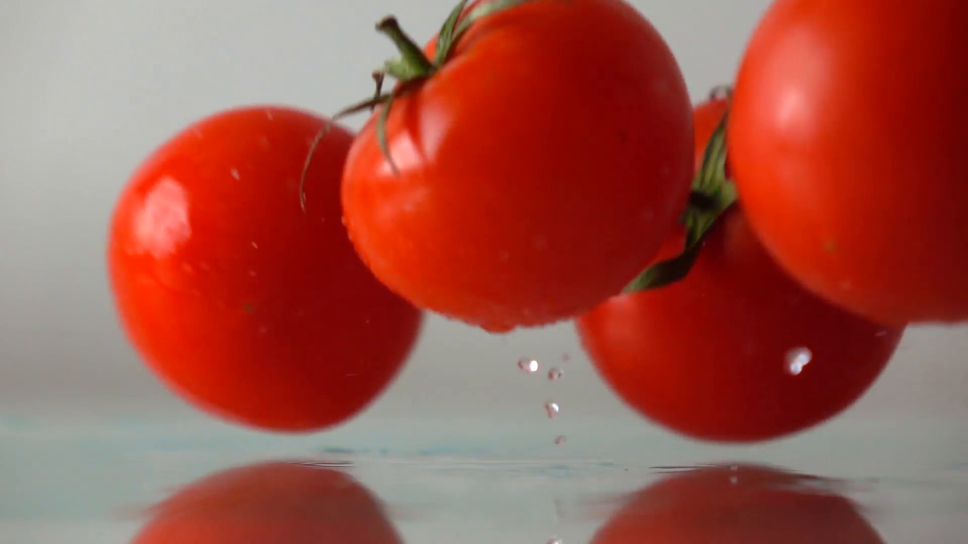 Red ripe tomatoes hit wet glass surface with splashes and rebound ...