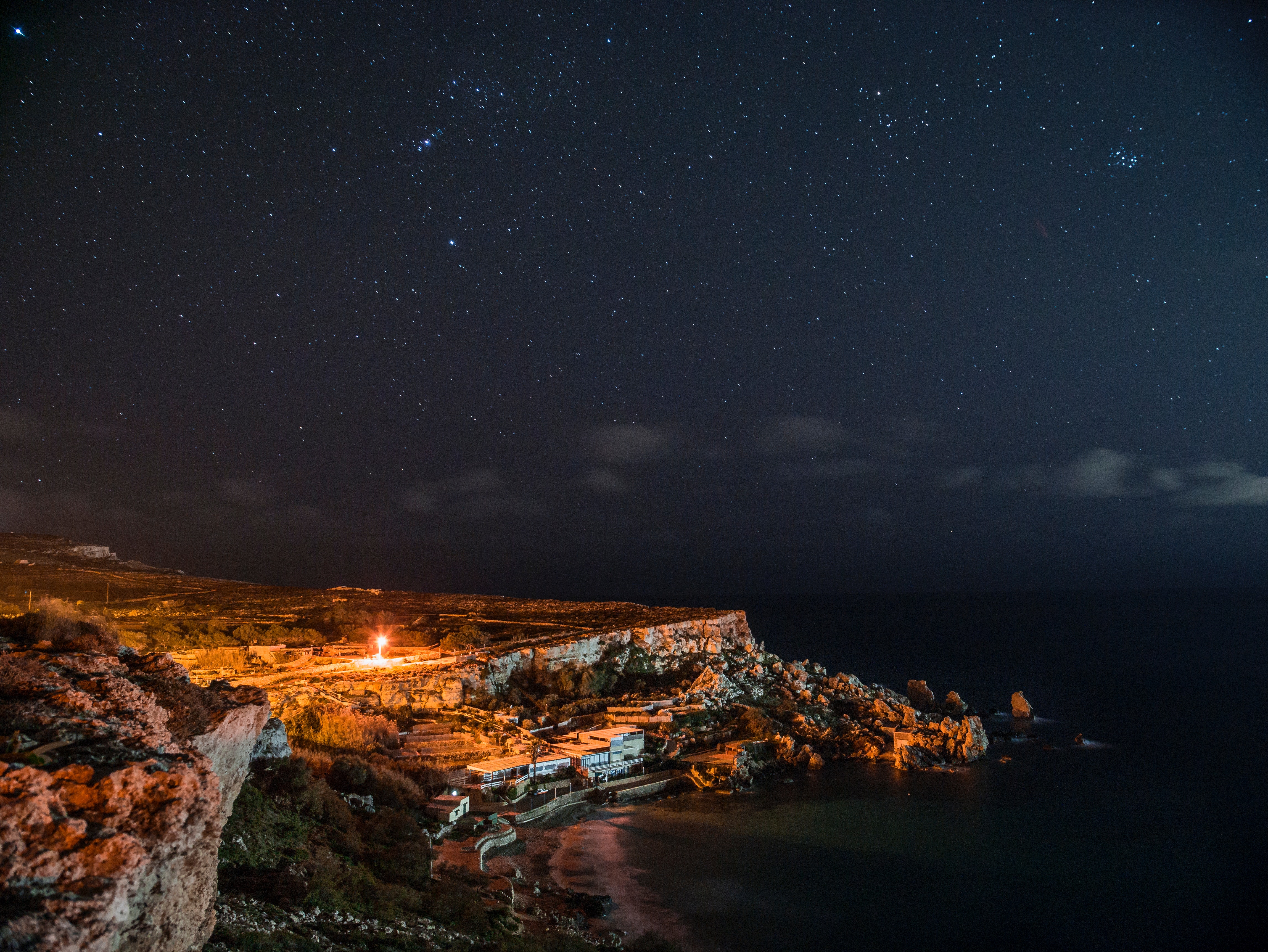 Rock cliff near body of water under clouds and sky during nighttime photo