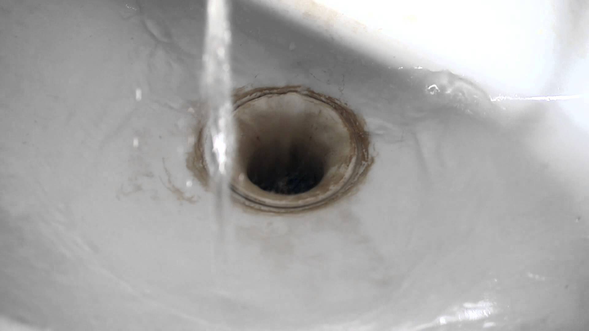 Drain hole of an old sink with rusted stains sucks up running water ...