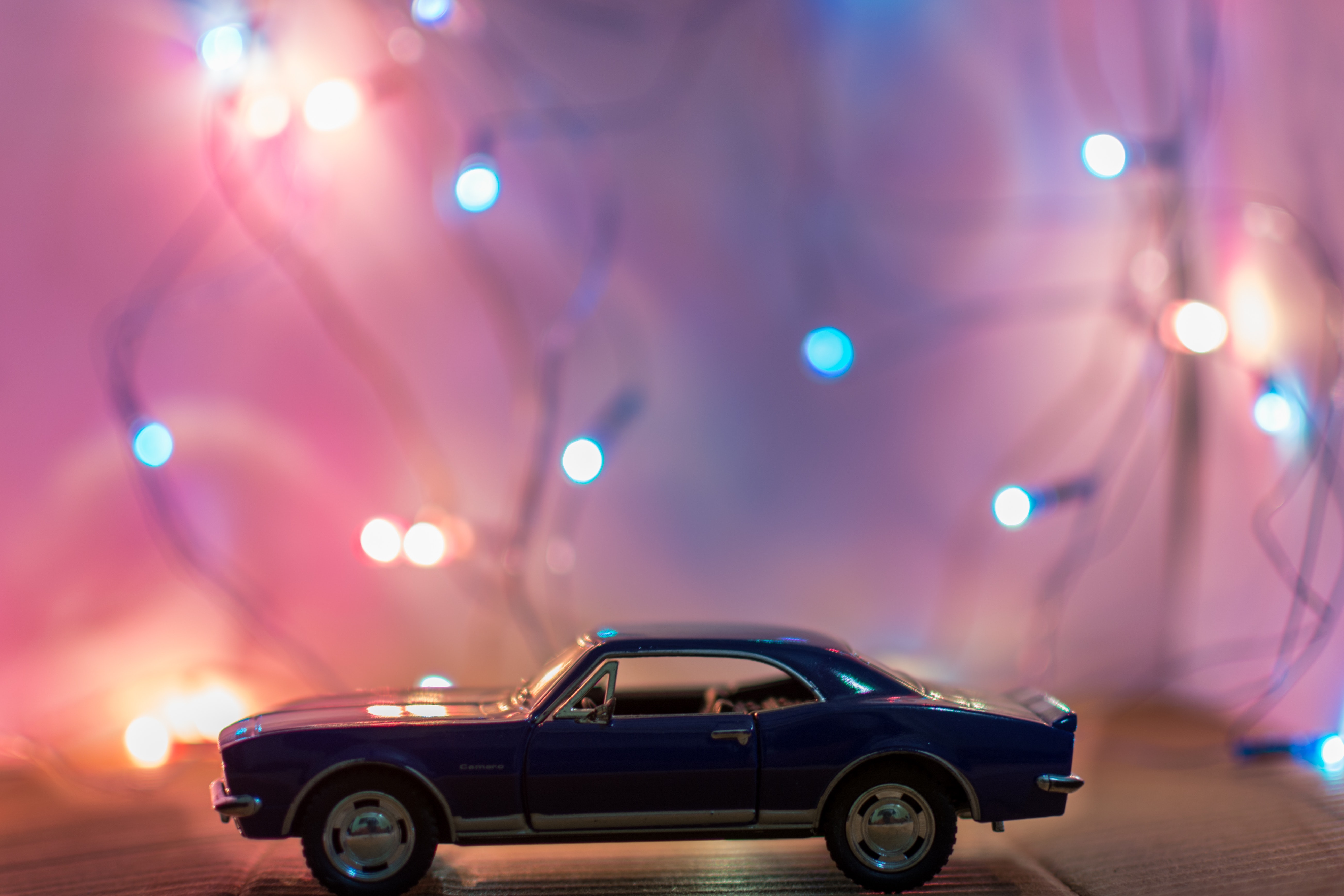 Selective focus photography of classic blue coupe die-cast model in front of string lights on table