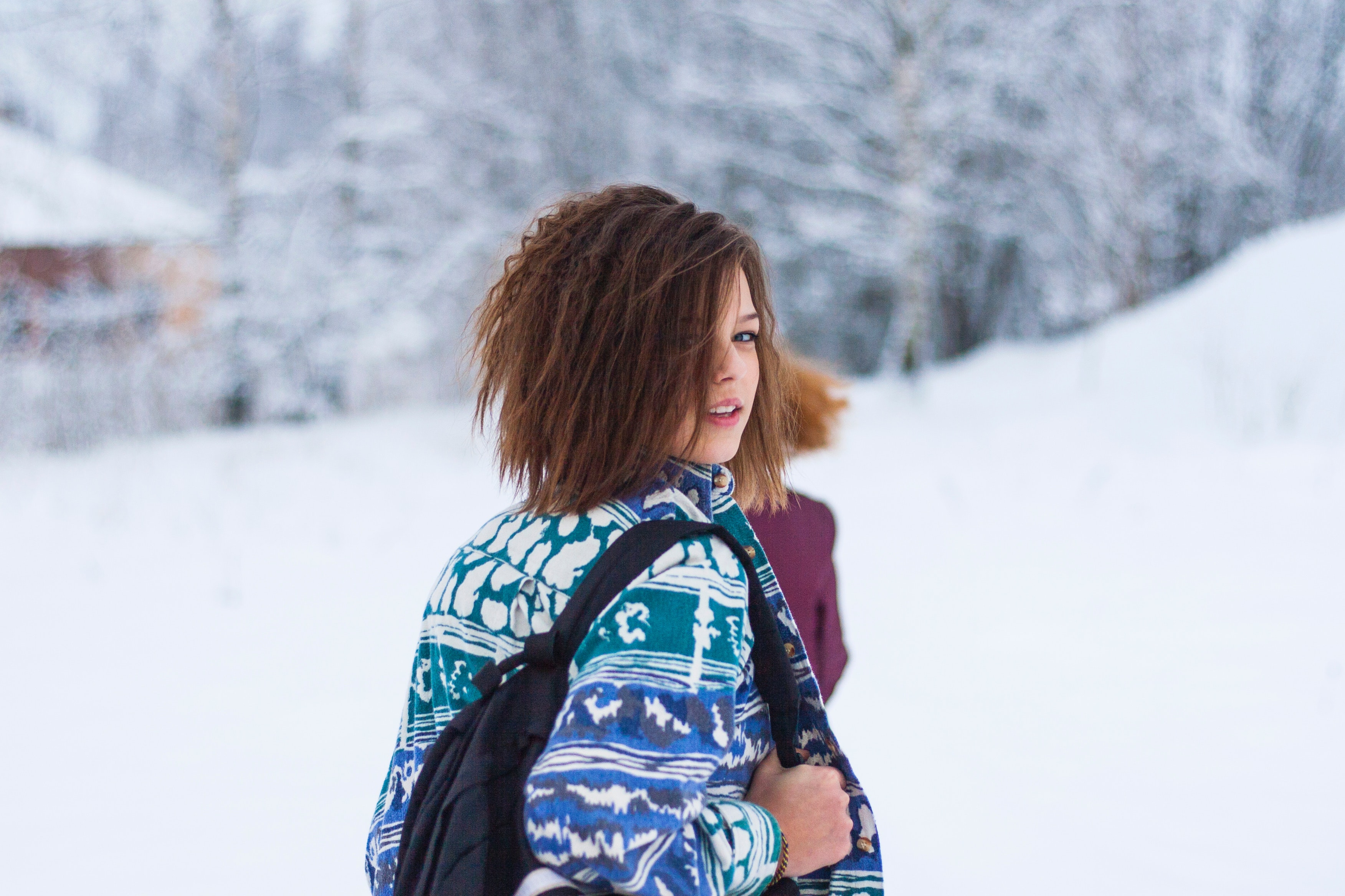 Selective focus portrait photograph of woman wearing blue, green, and white tribal jacket and black backpack outfit