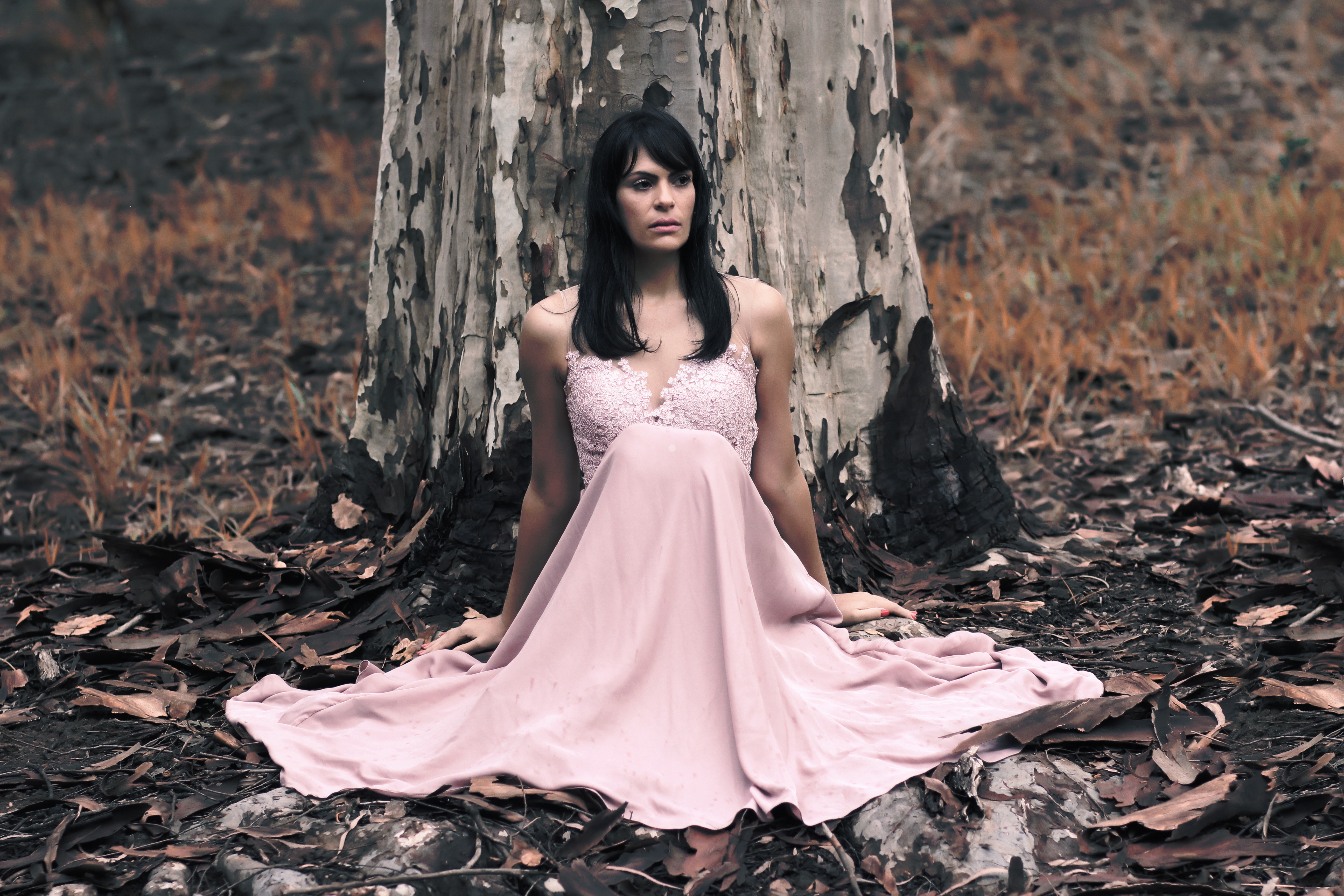Shallow focus photography of black haired woman in pink sleeveless dress sitting in front of tree