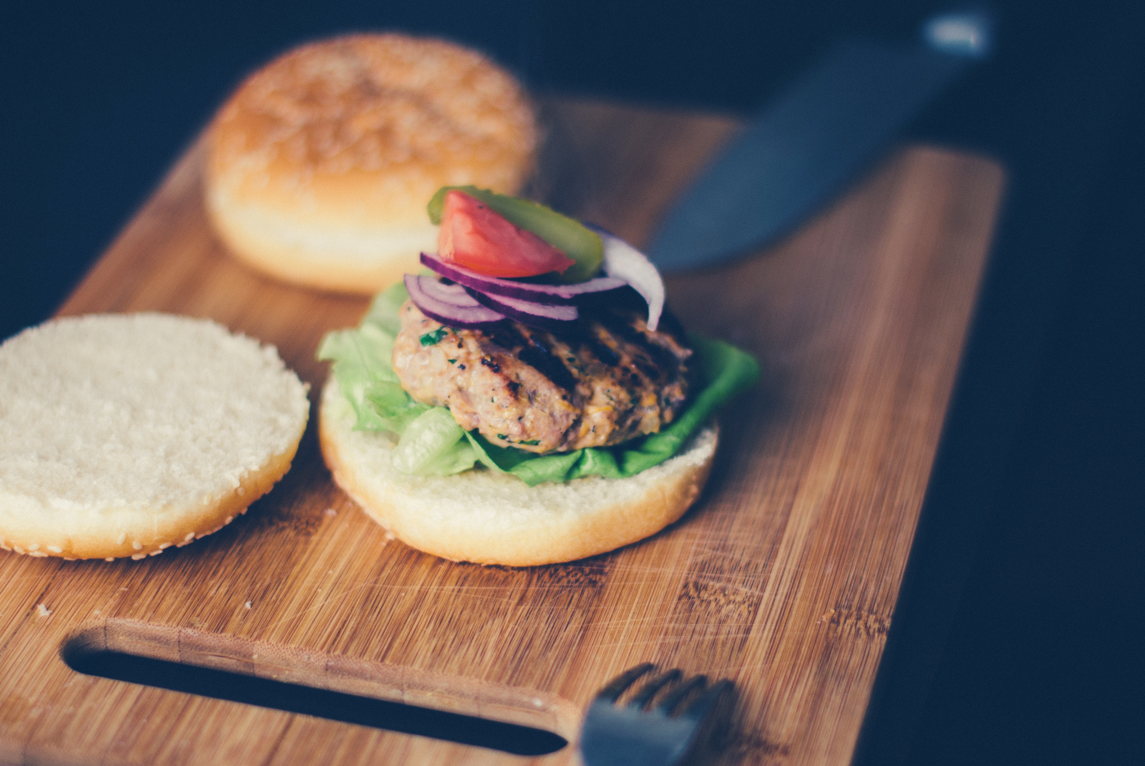Shallow focus photography of burger sandwich served on brown wooden chopping board