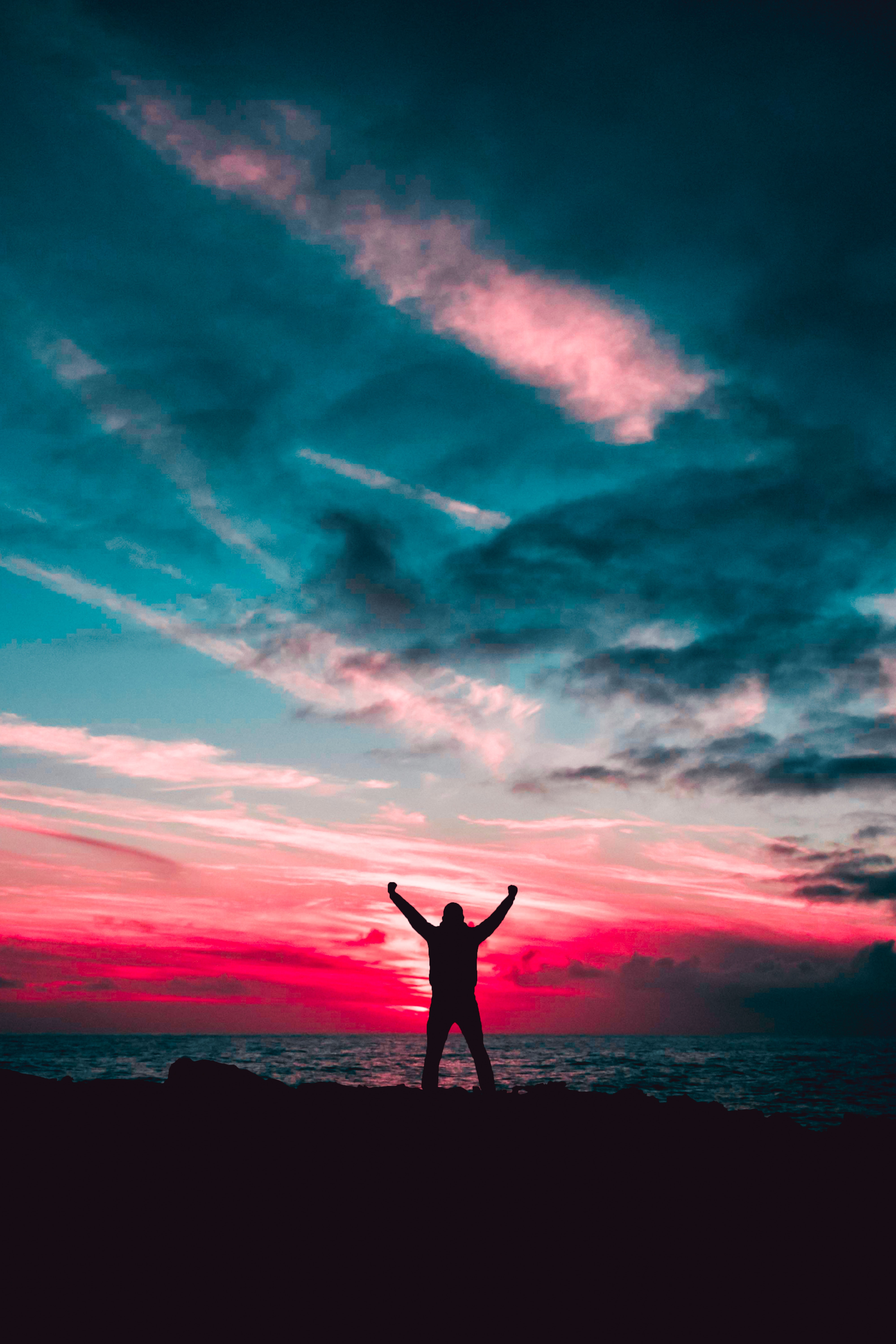 Silhouette of man raising hands against a red sunset light under green clouds photo