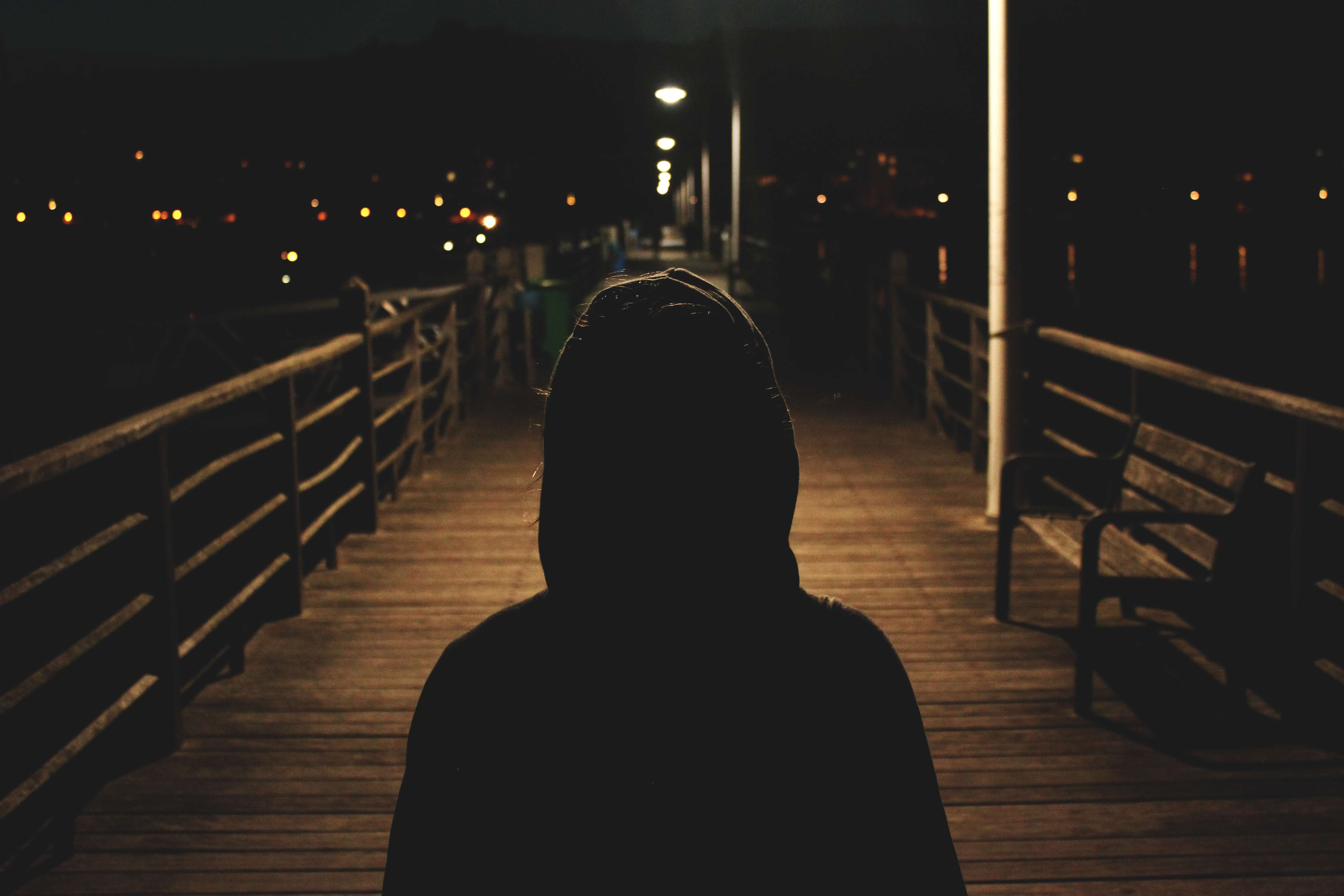 Silhouette of person in hoodie on boardwalk at night photo
