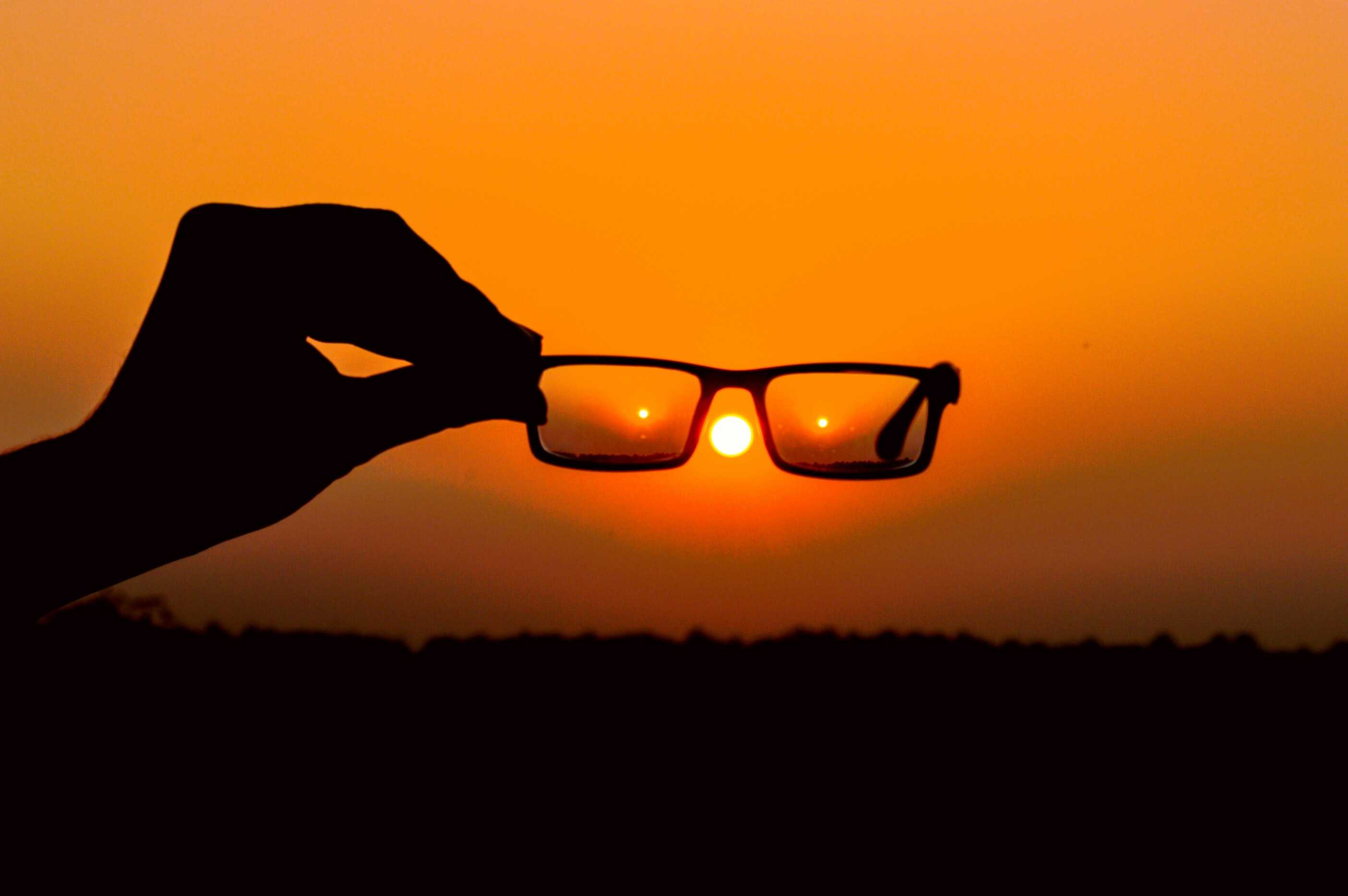 Silhouette of person's hand holding eyeglasses during golden hour photo