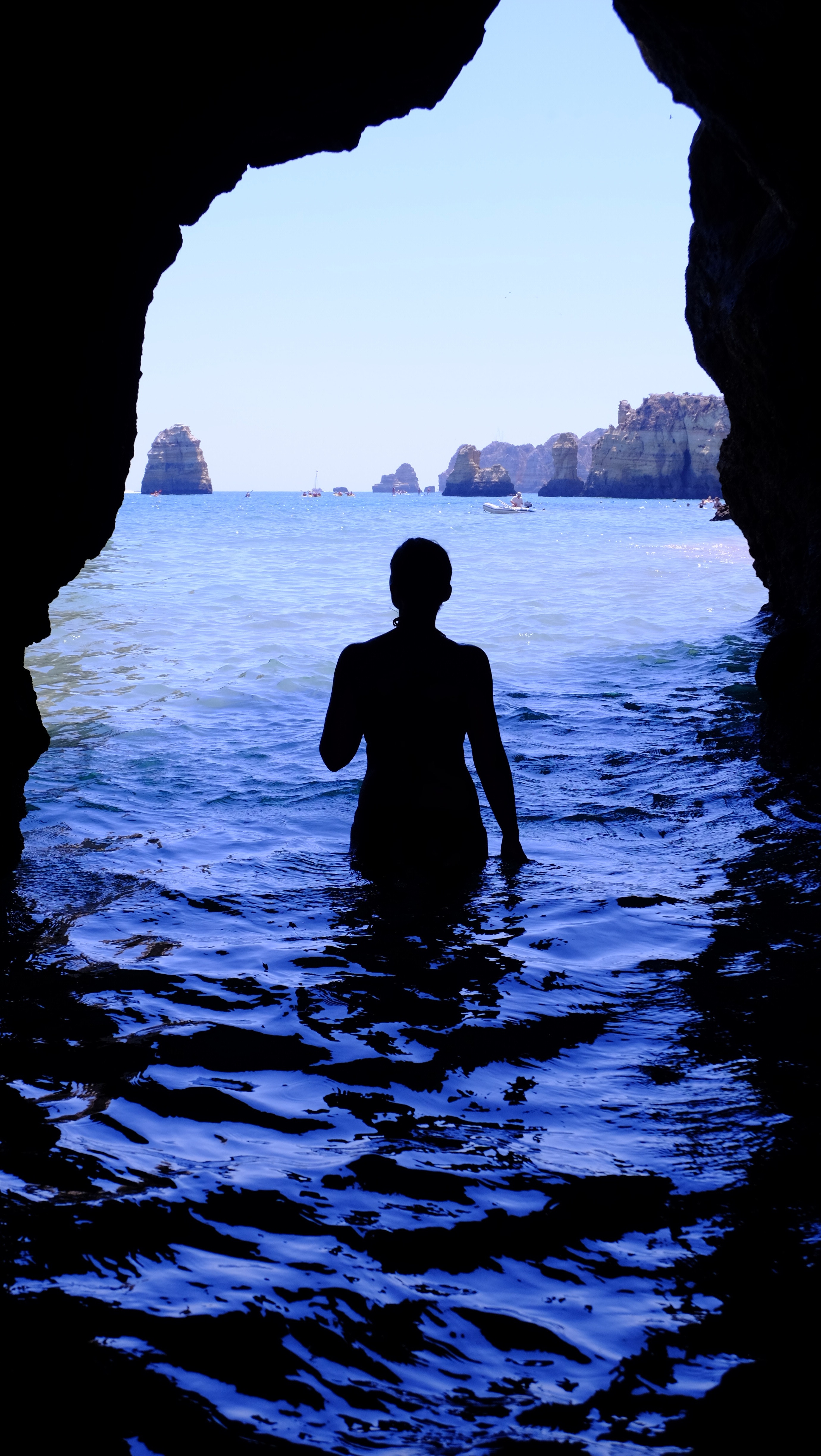 Silhouette of woman at blue sea inside black cave during daytime photo