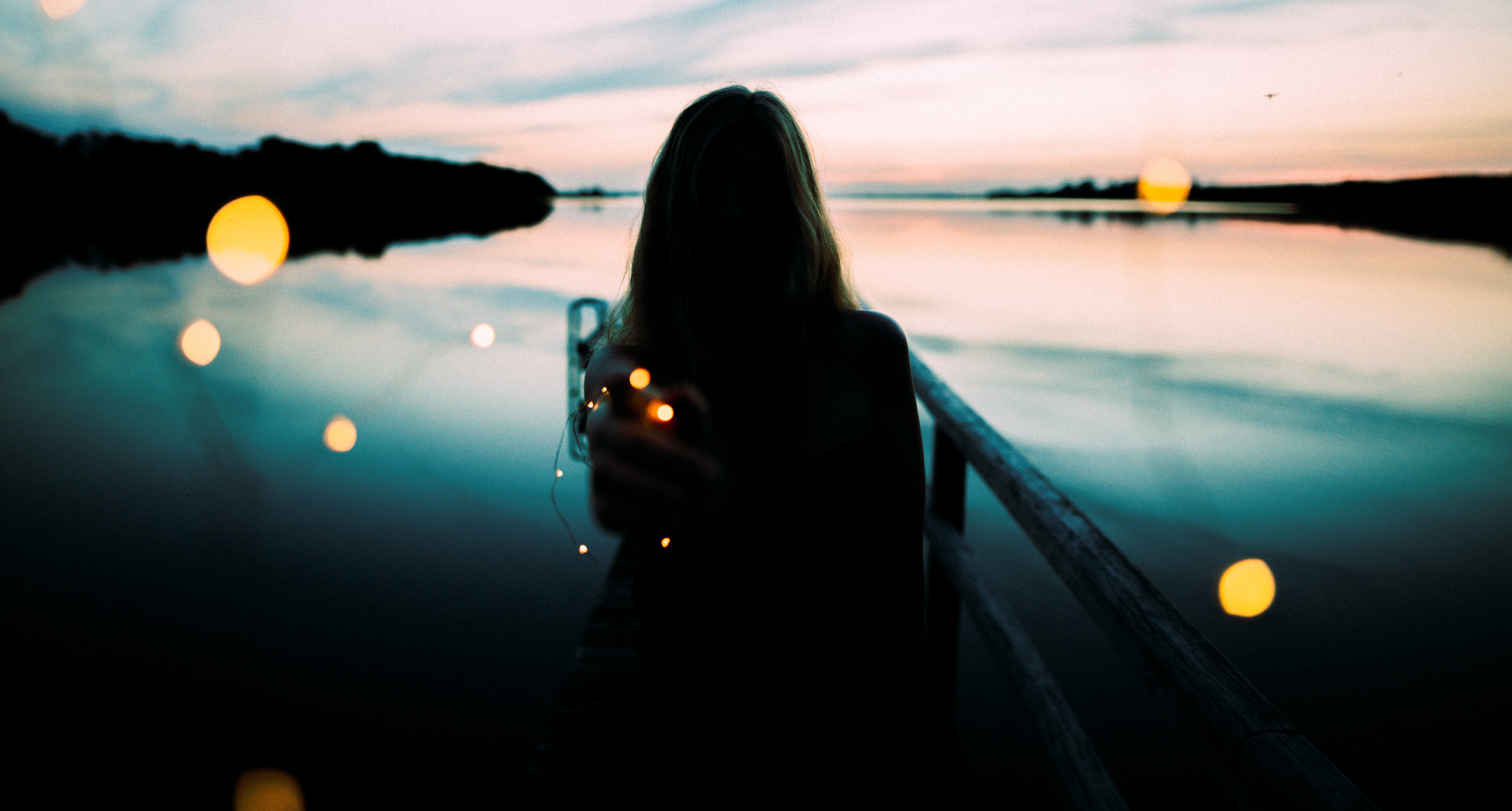 Silhouette of woman leaning on metal railings with background of body of water by the shoreline photo