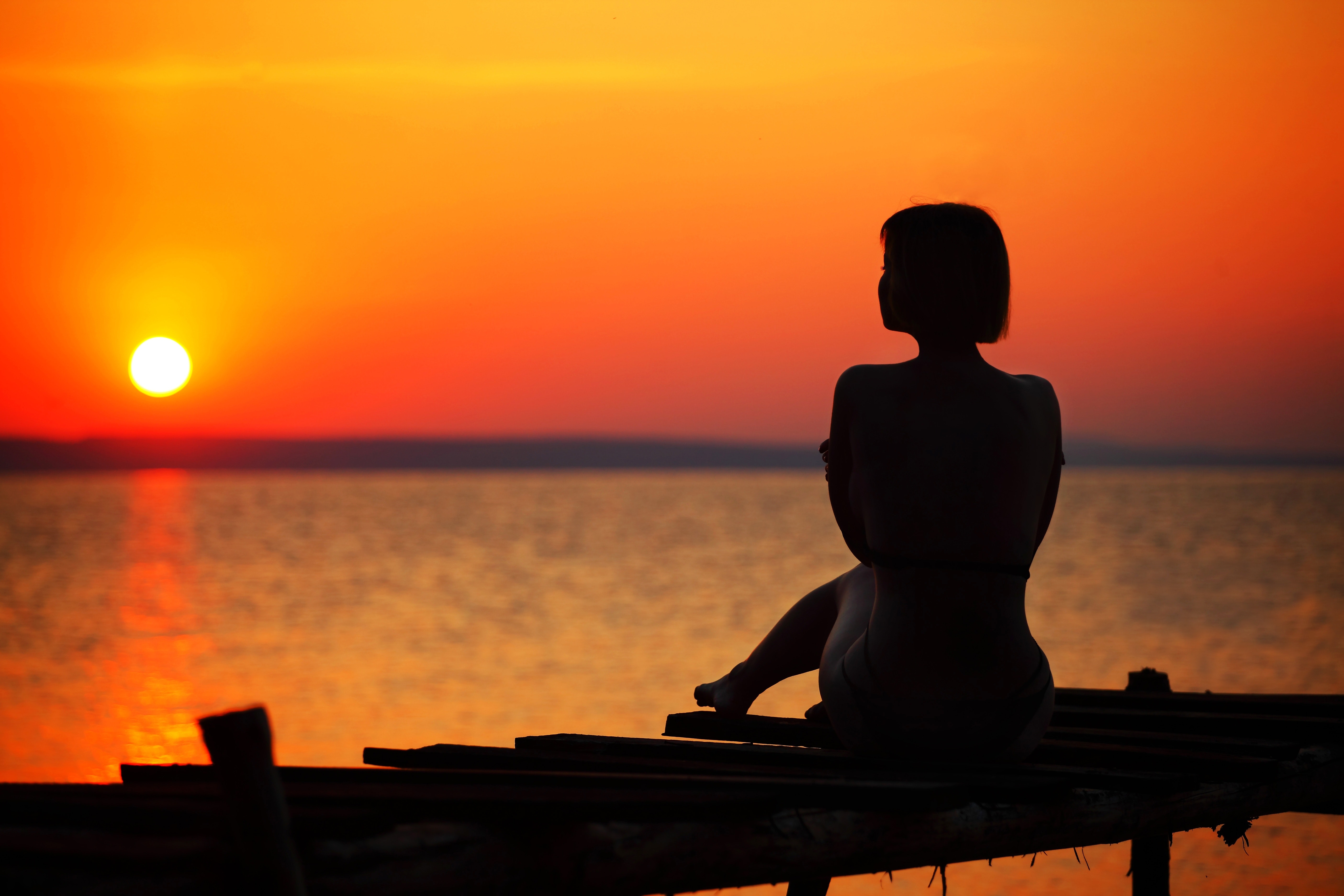 Silhouette of woman sitting on dock during sunset photo