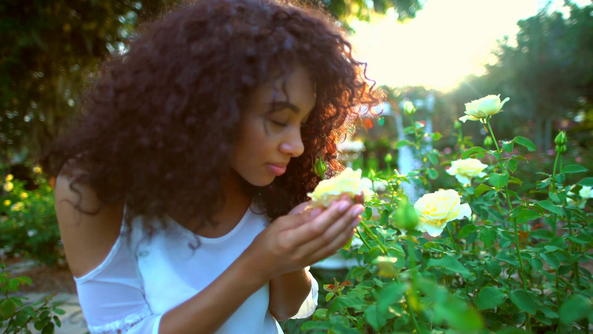 Young cute African American girl smelling the flowers in the garden ...