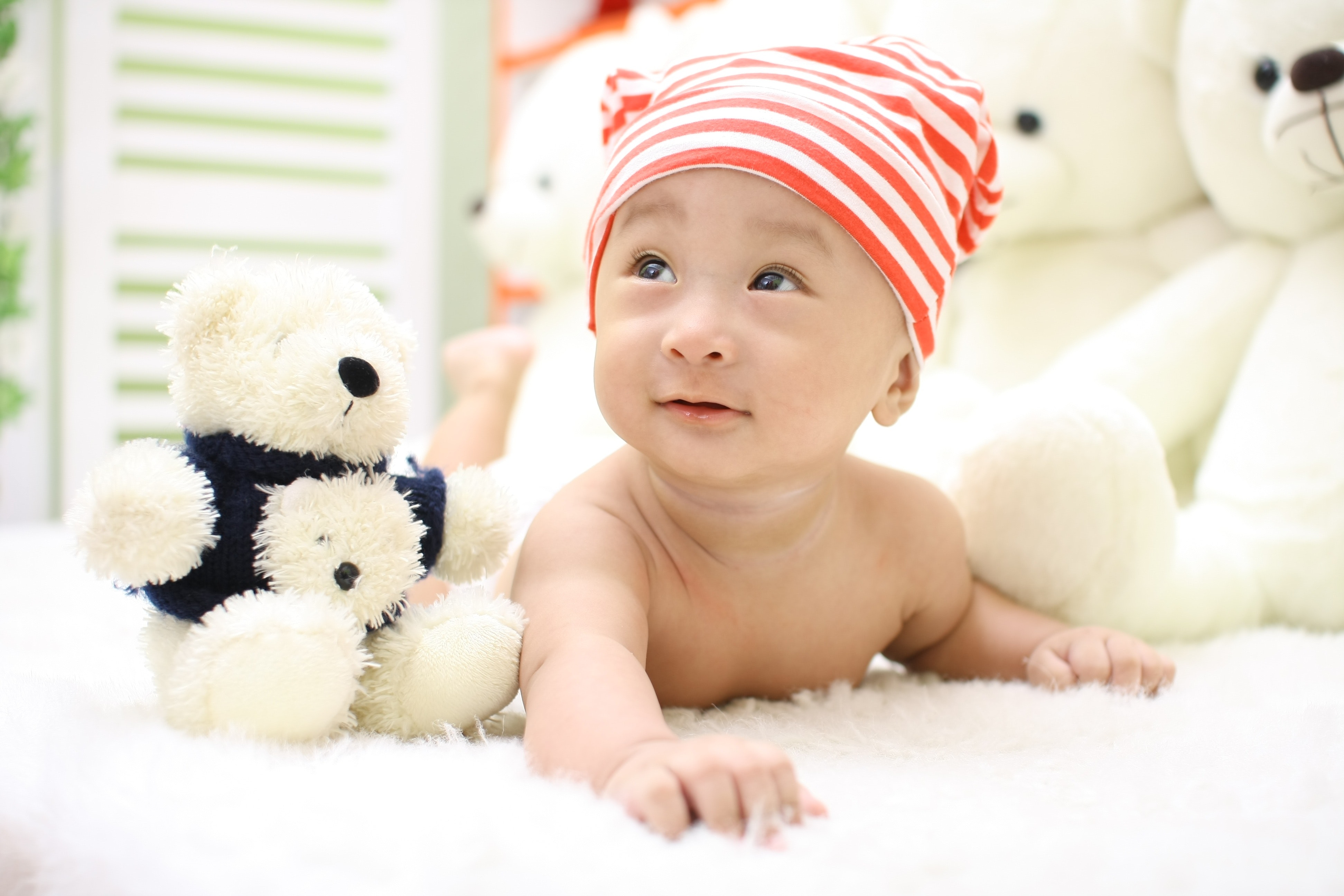 Smiling toddler wearing orange and white knit cap beside black and white bear plush toy photo