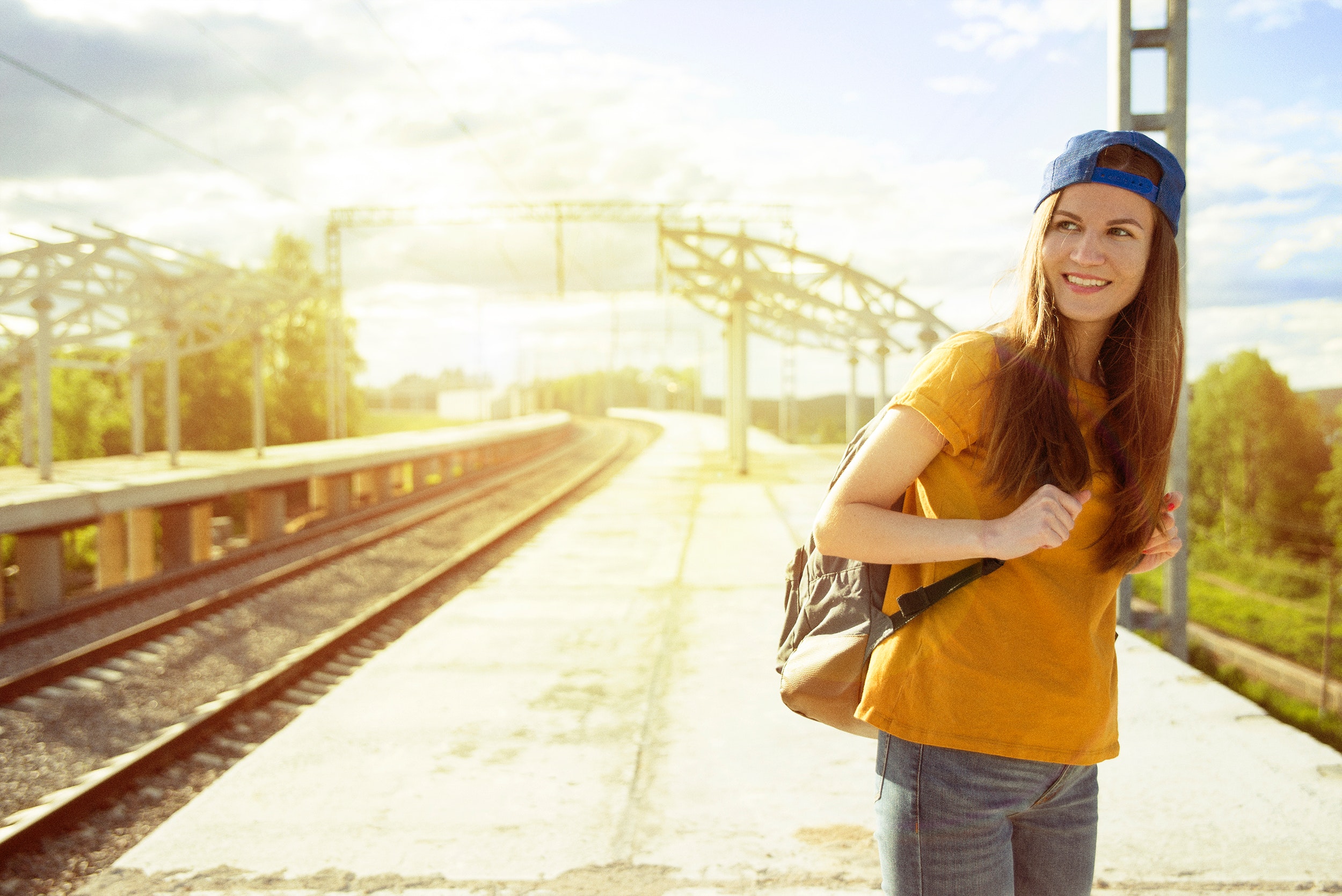 Smiling woman in orange t shirt and blue snap back cap carrying backpack photo