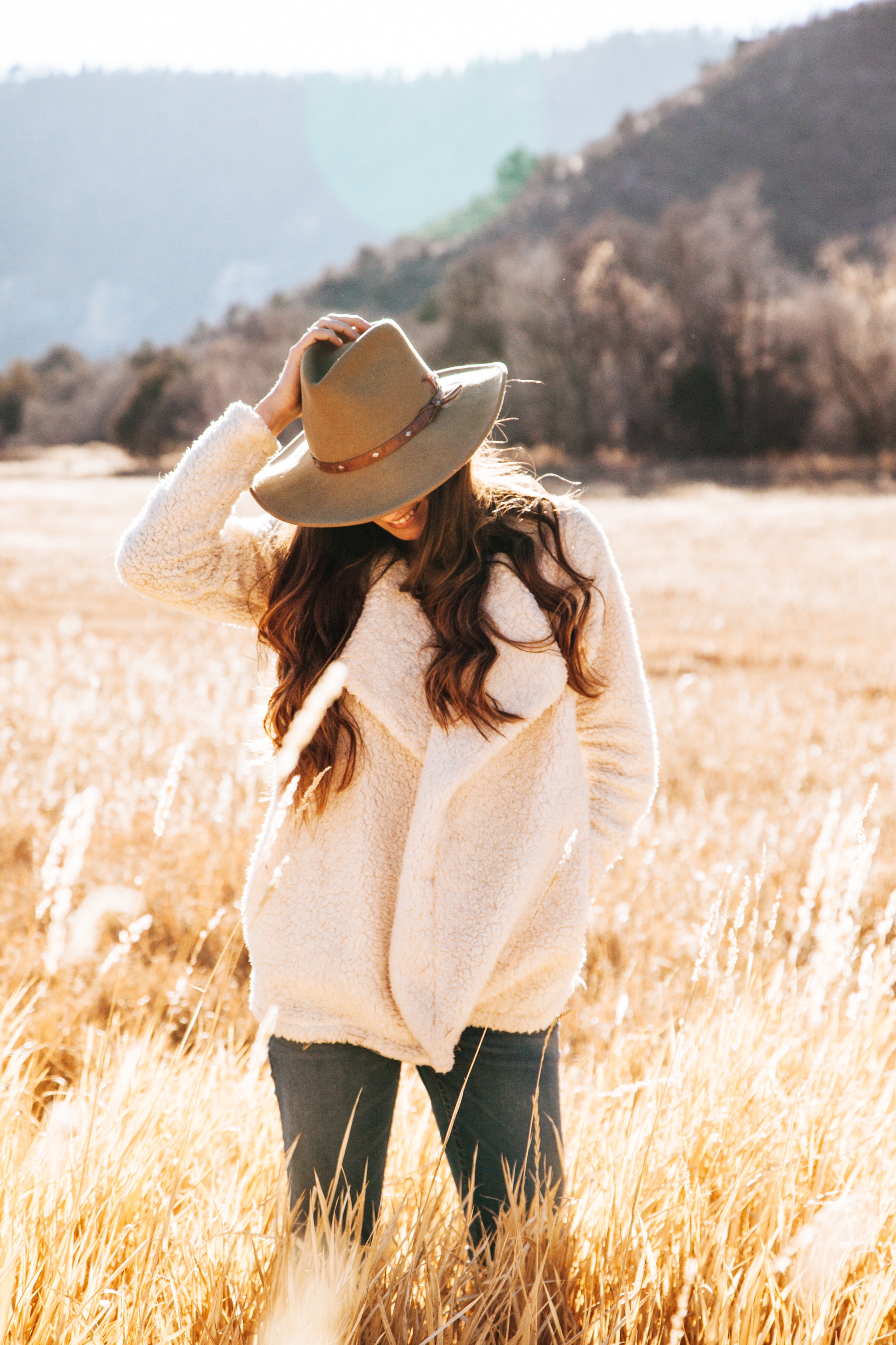 Smiling woman in white winter jacket wearing brown cowboy hat surrounded of brown grass field photo