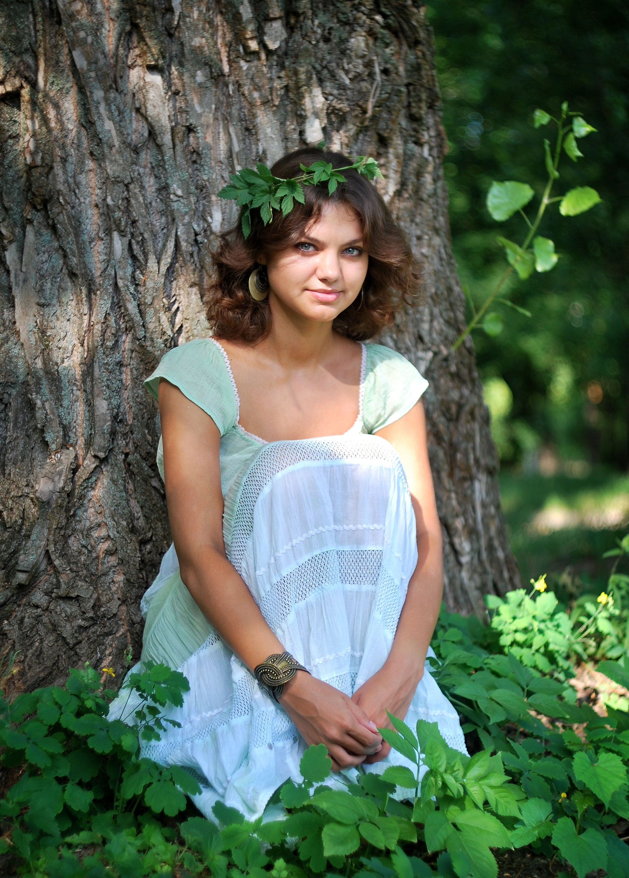 Smiling woman wearing green leaf crown with green and white sleeveless dress sitting in green leaf during day time photo