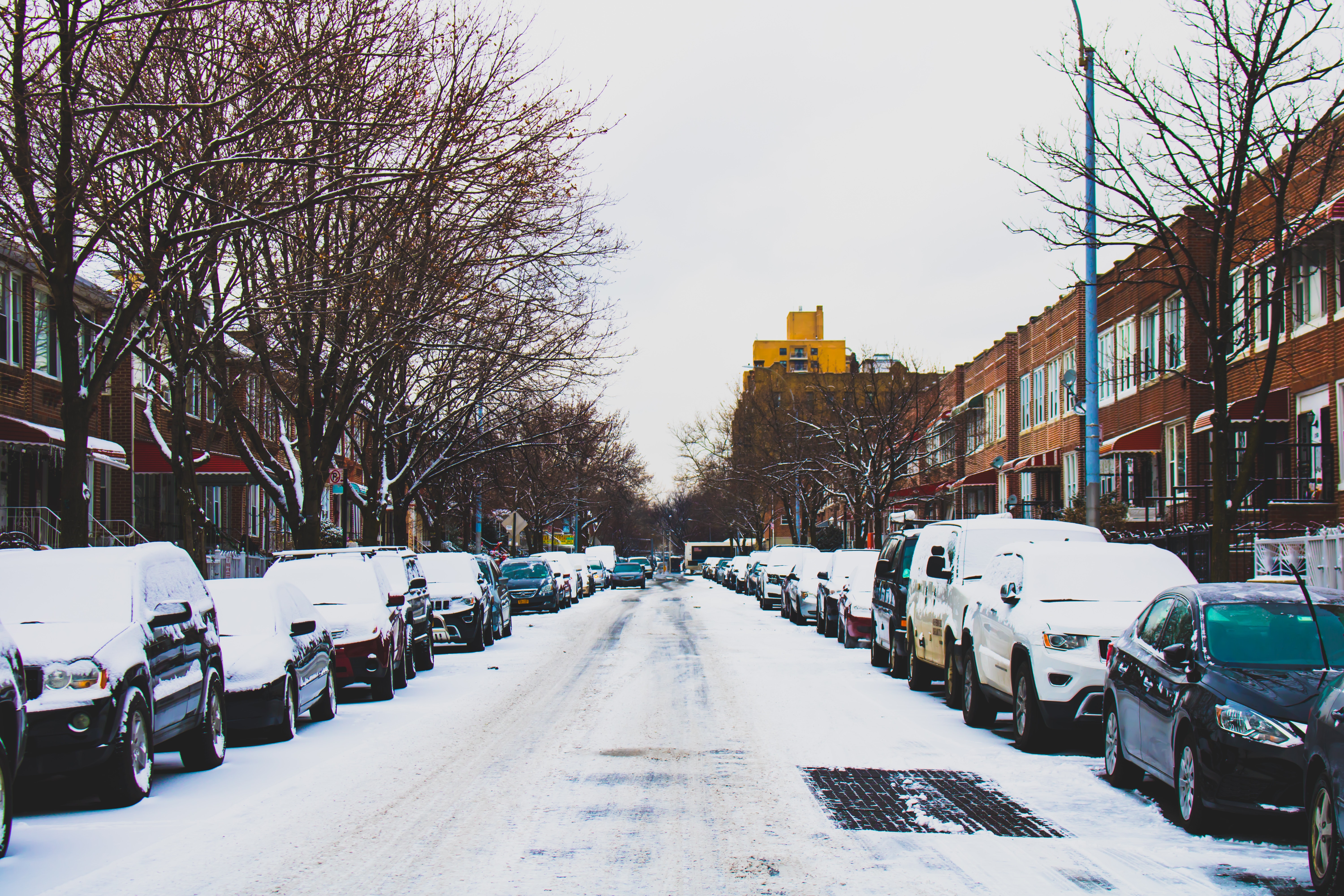 Snow covered road and inline parked vehicles between 2-storey buildings under white sky photo