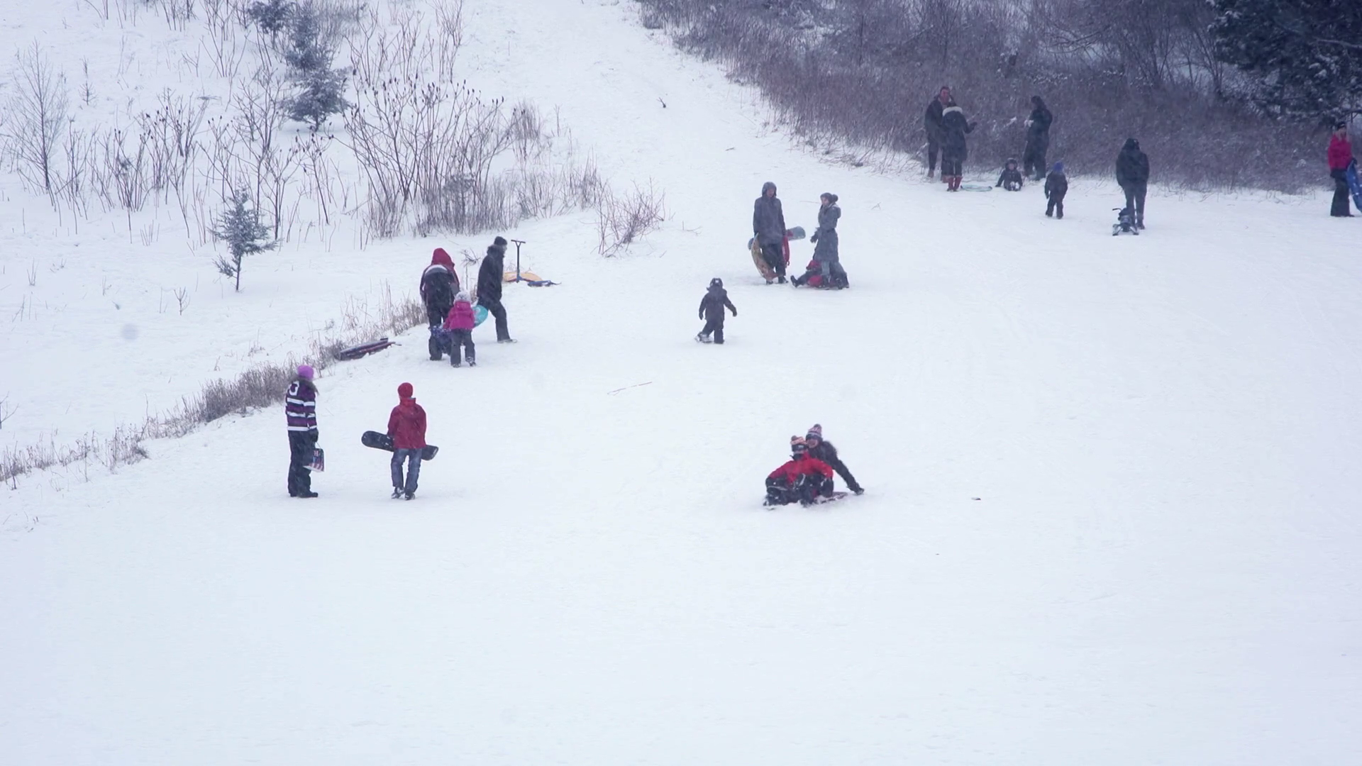 Kids and adults enjoying a small ski hill on a snowy day in suburban ...