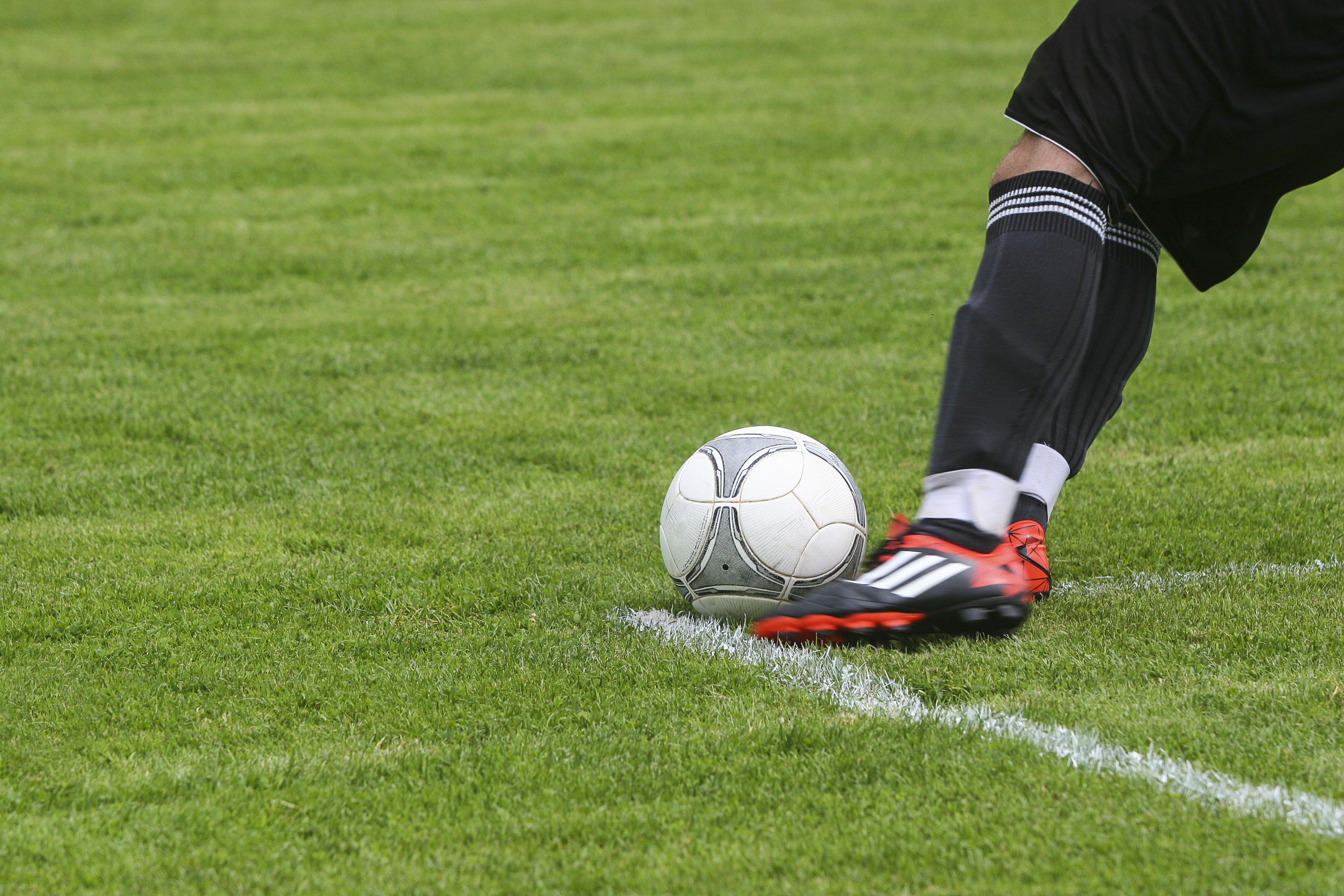 Soccer player kicking white gray soccer ball on green grass field photo