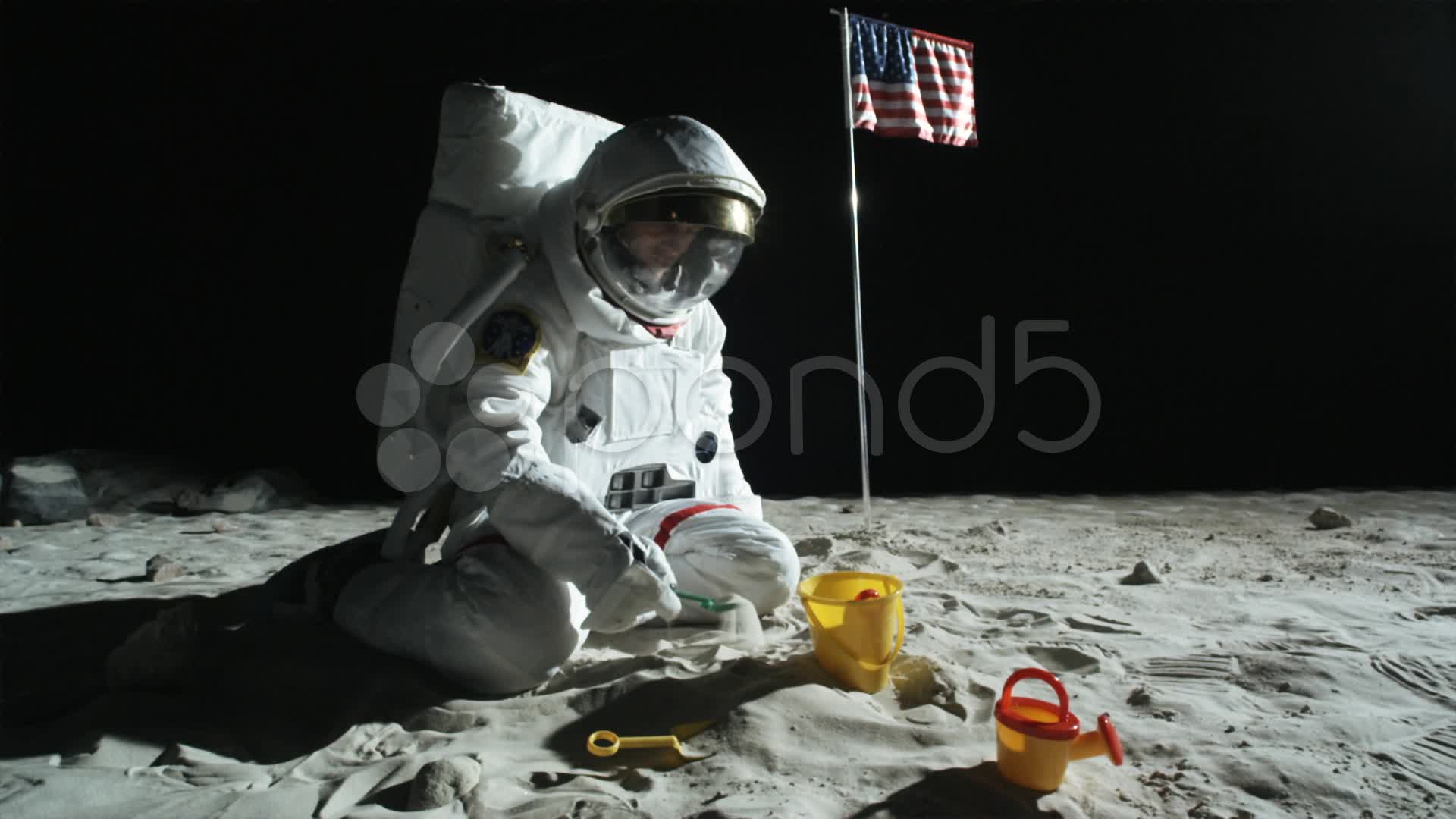 SLO MO, WS, ZO of an astronaut sitting on the moon's surface playing ...