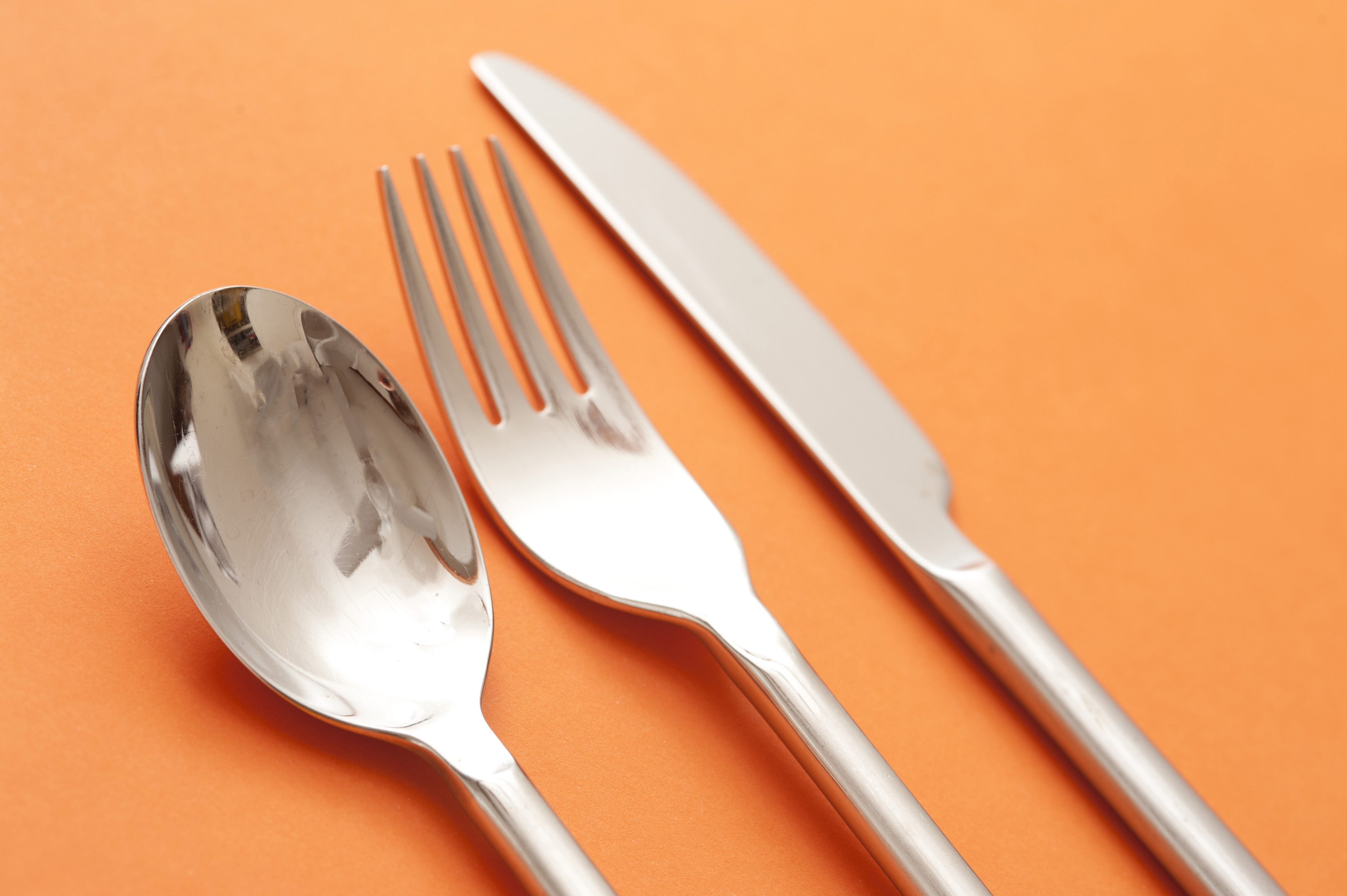 Image of Silver Spoon, Fork, and Knife on Orange Background ...