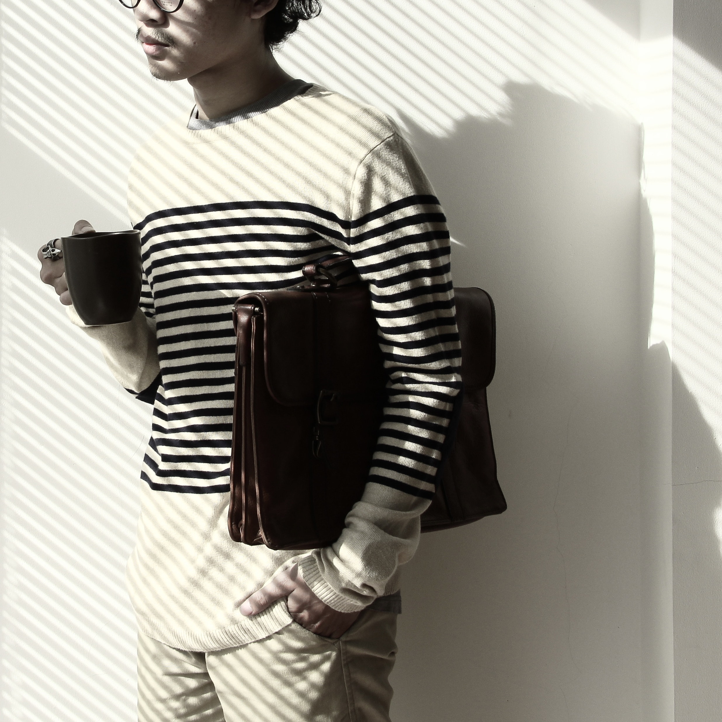 Standing brunet person waring eyeglasses and white black stripe sweater holding mug and briefcase photo