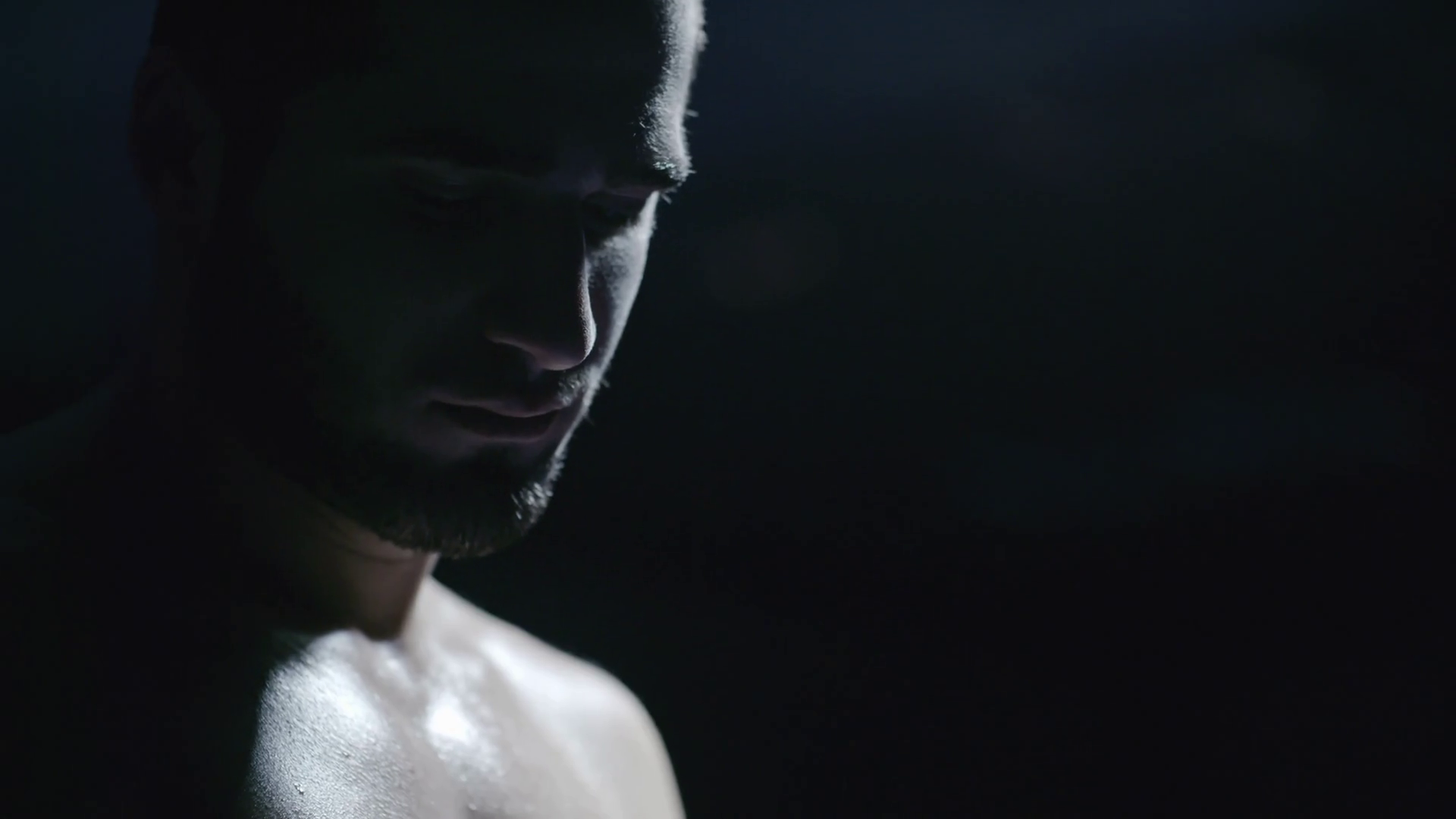 Close up of face of shirtless athlete standing in dark gym and ...