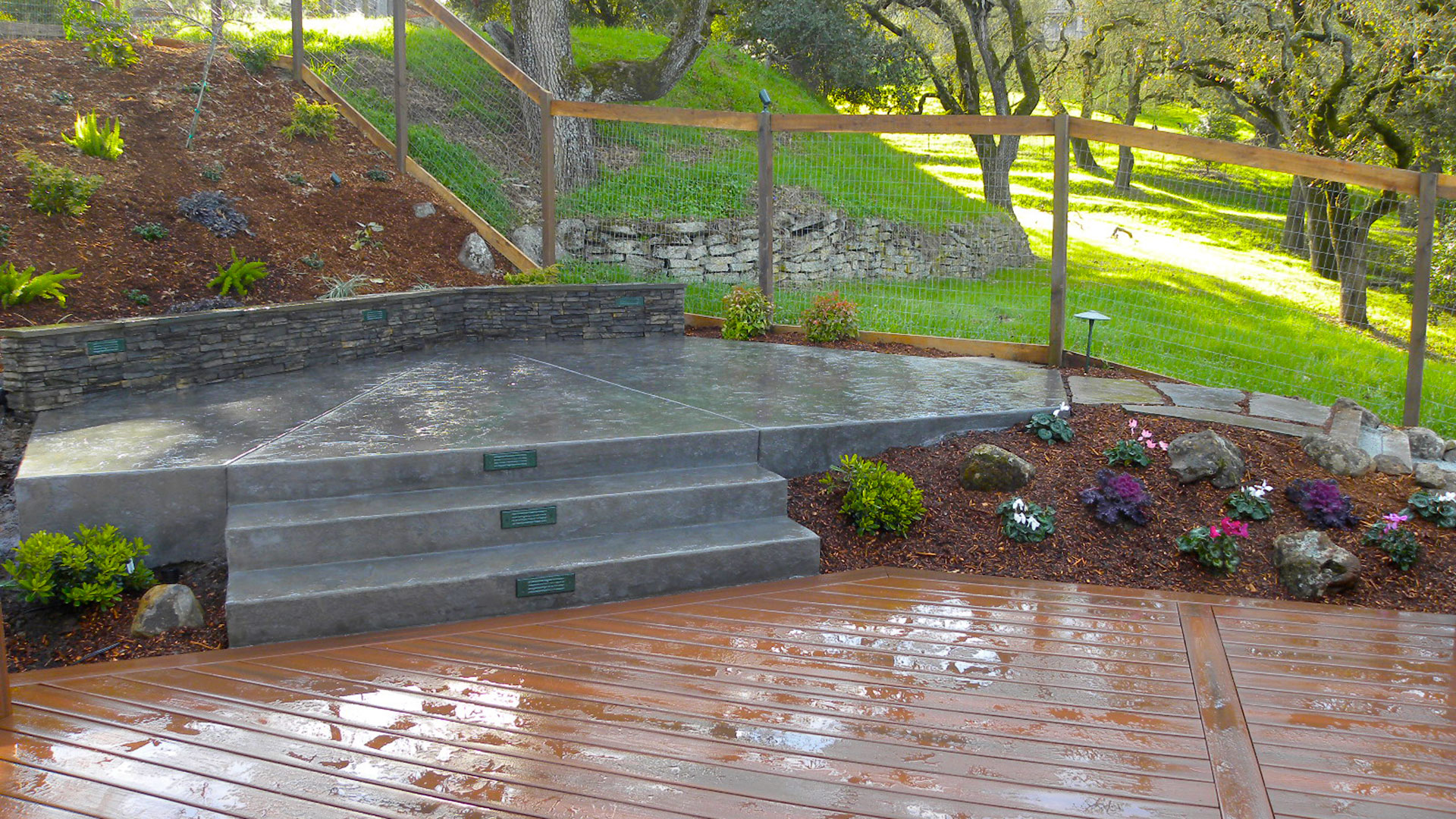 Stamped concrete patio, framed by a ledgestone seat wall, steps down ...