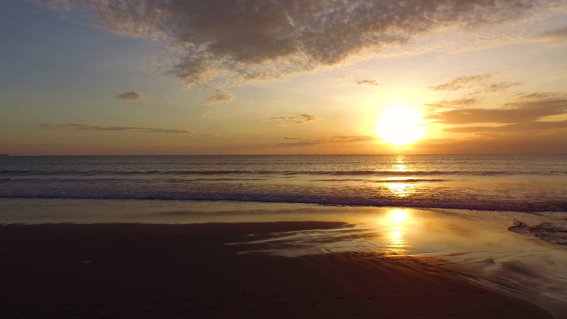Gliding drone shot toward serene sunset over beach and ocean waves ...