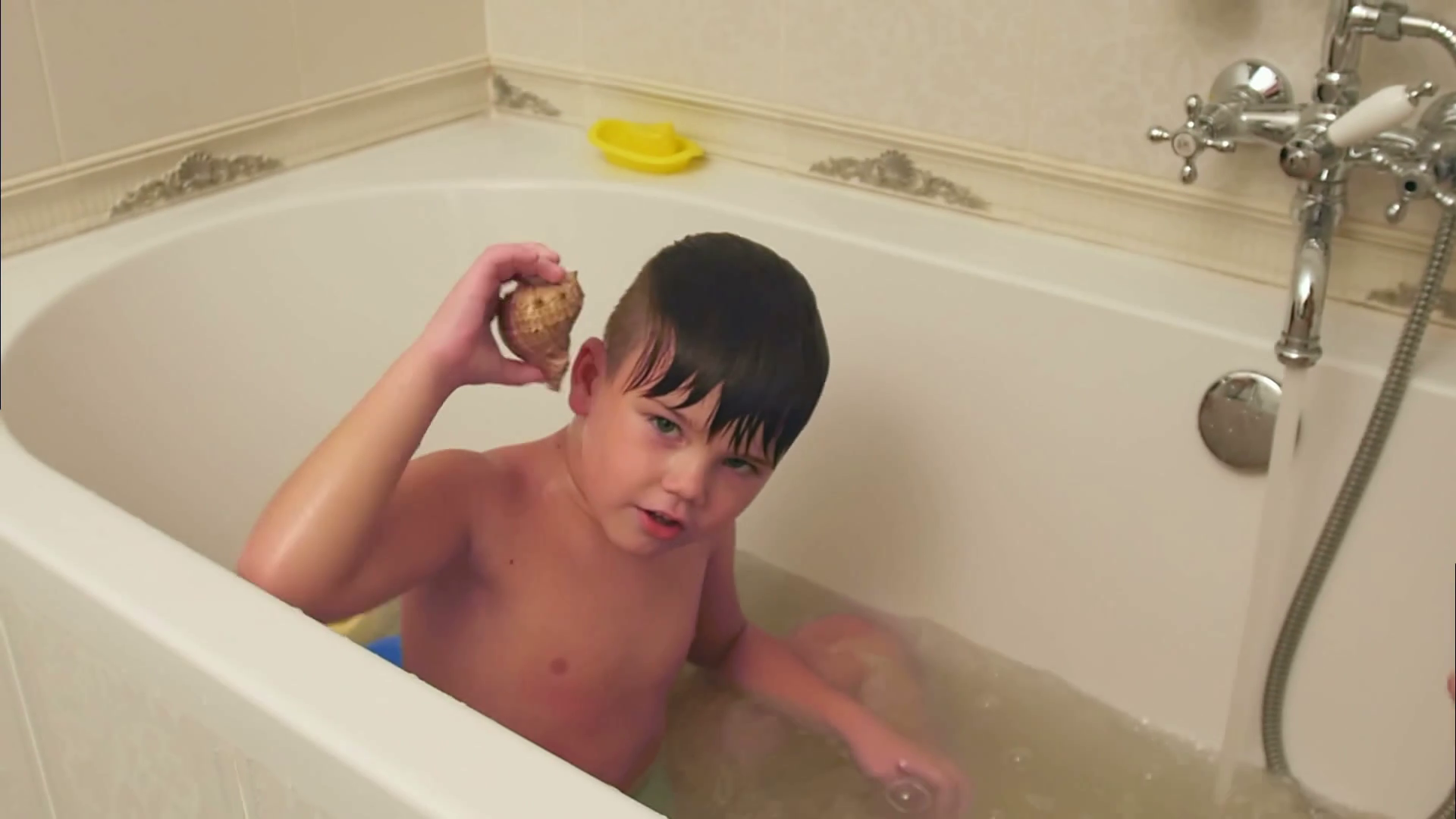 Little boy playing with seashell while taking bath in bathtub Stock ...