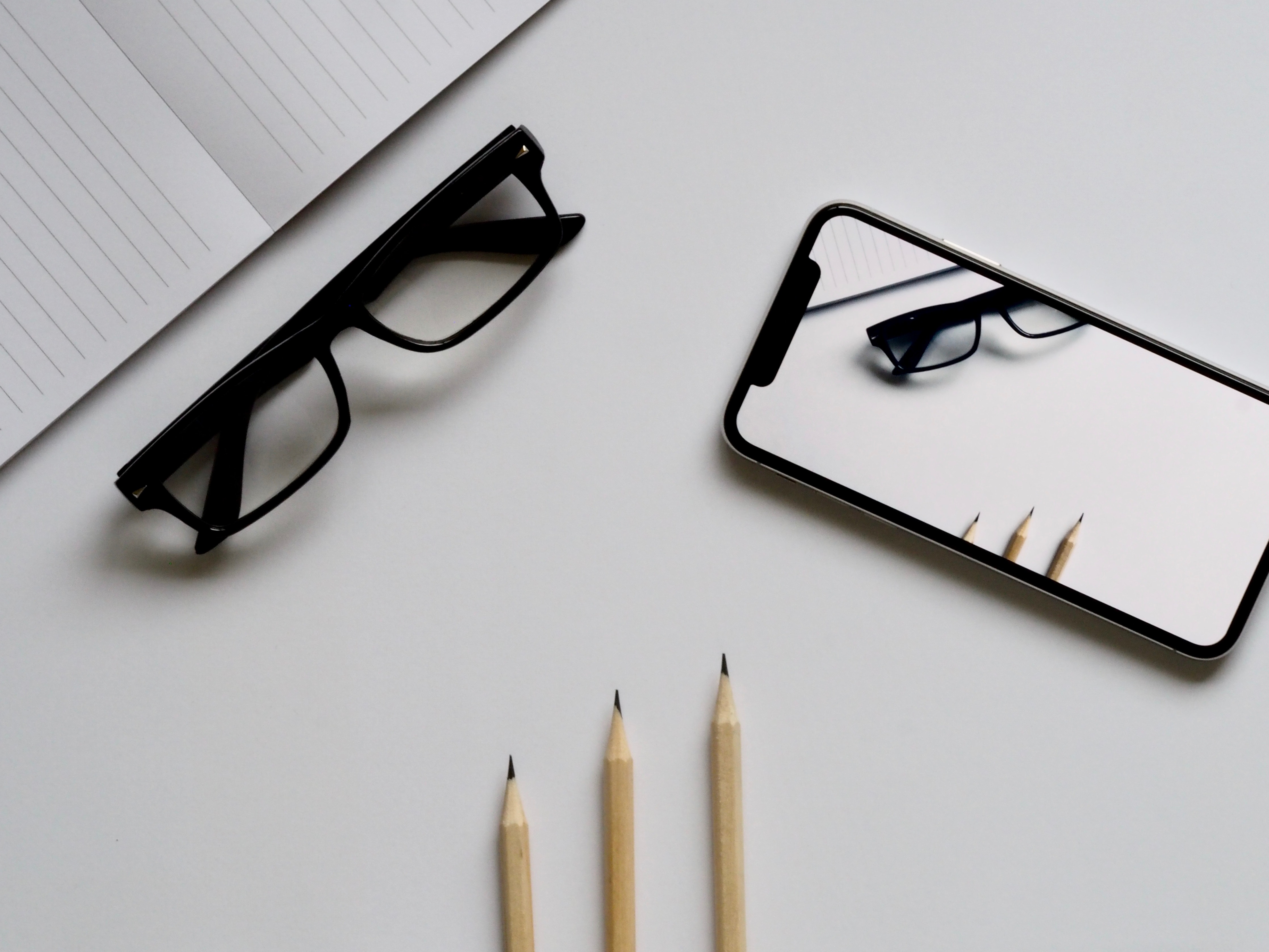 Three pencils, eyeglasses, and smartphone on white table photo