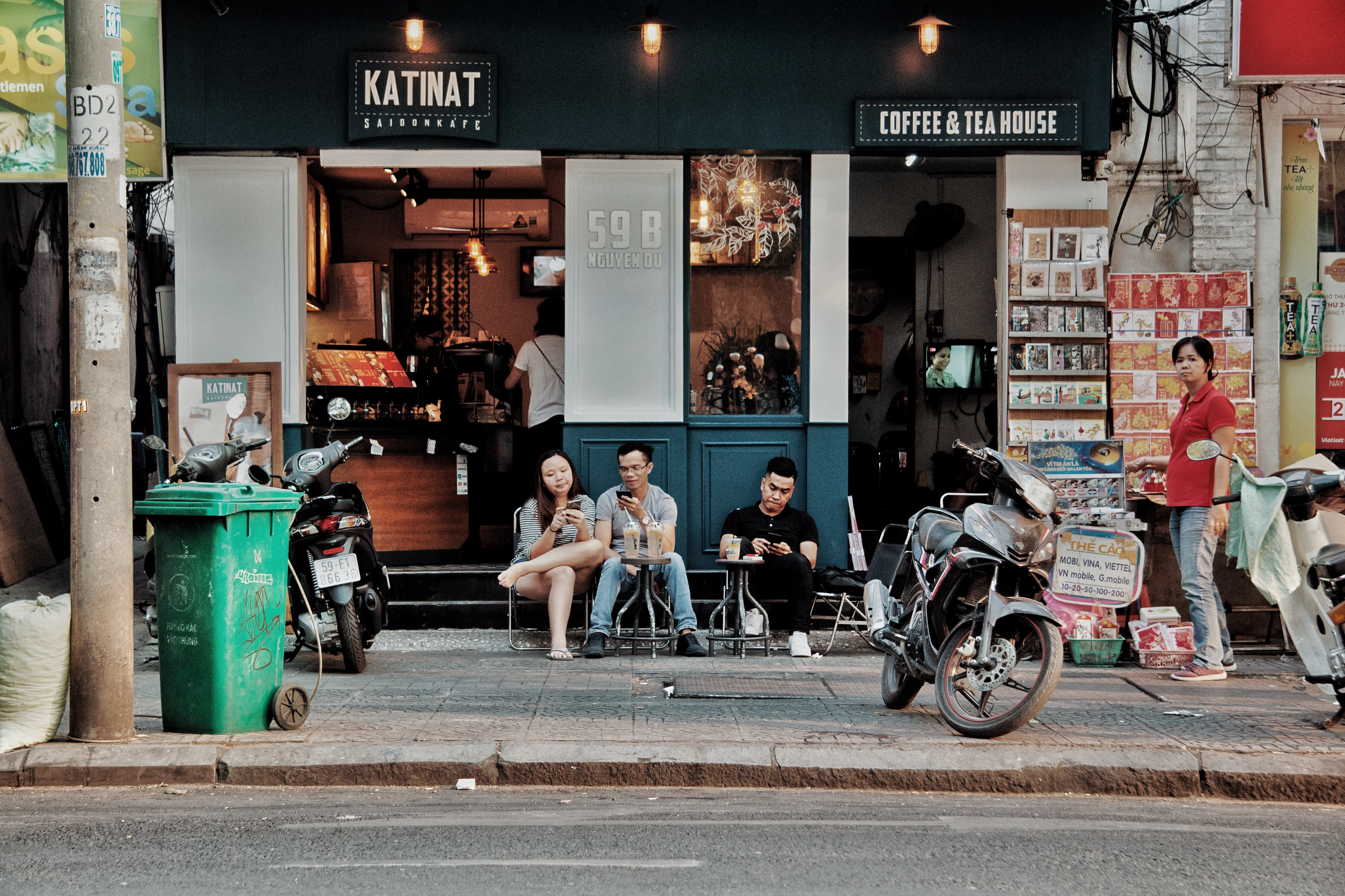 Three people sitting on chairs outside coffee & tea house near motorcycles photo