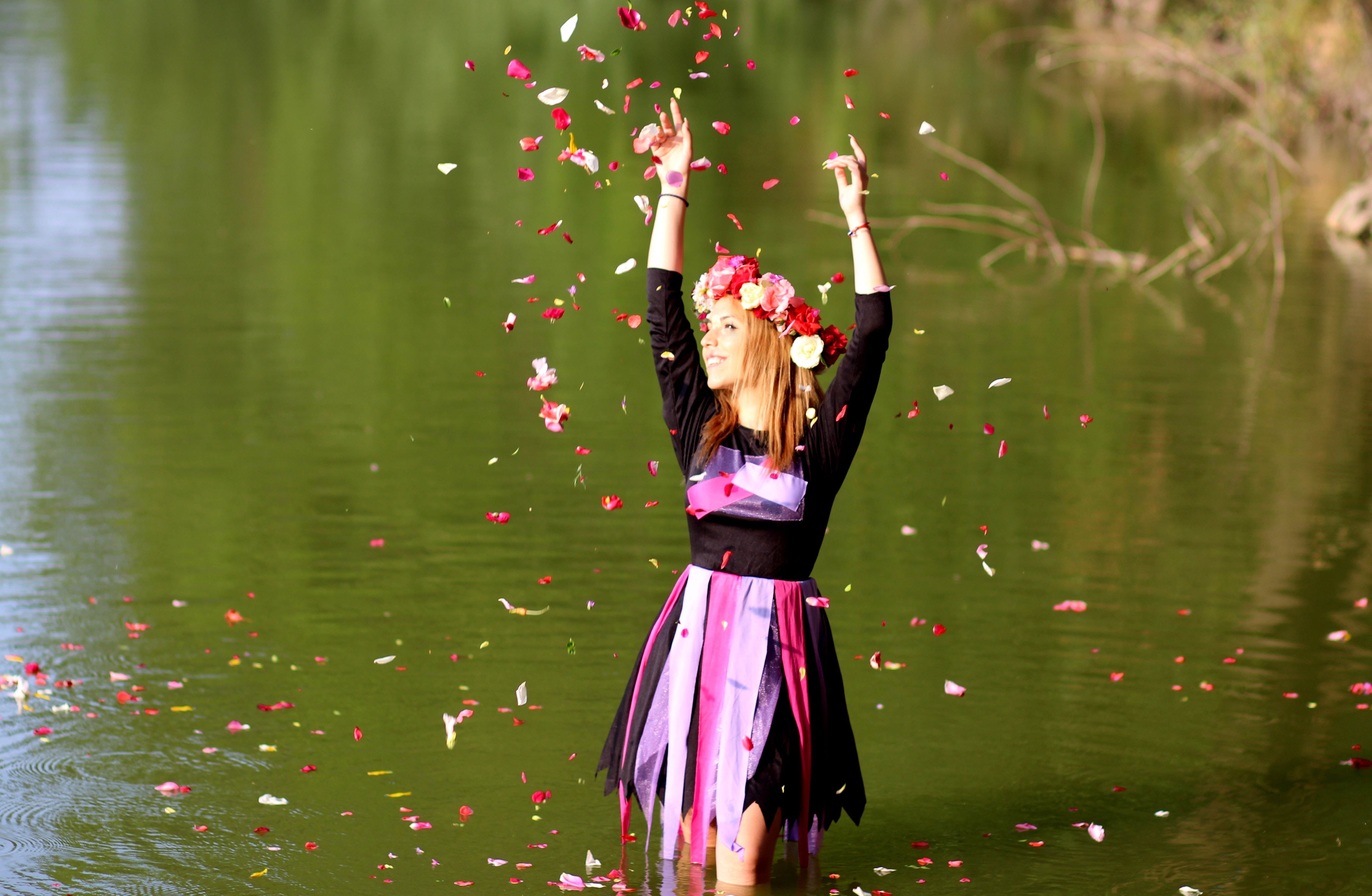 Time lapse photo of woman standing in green body of water while pouring flower petals on air during daytime