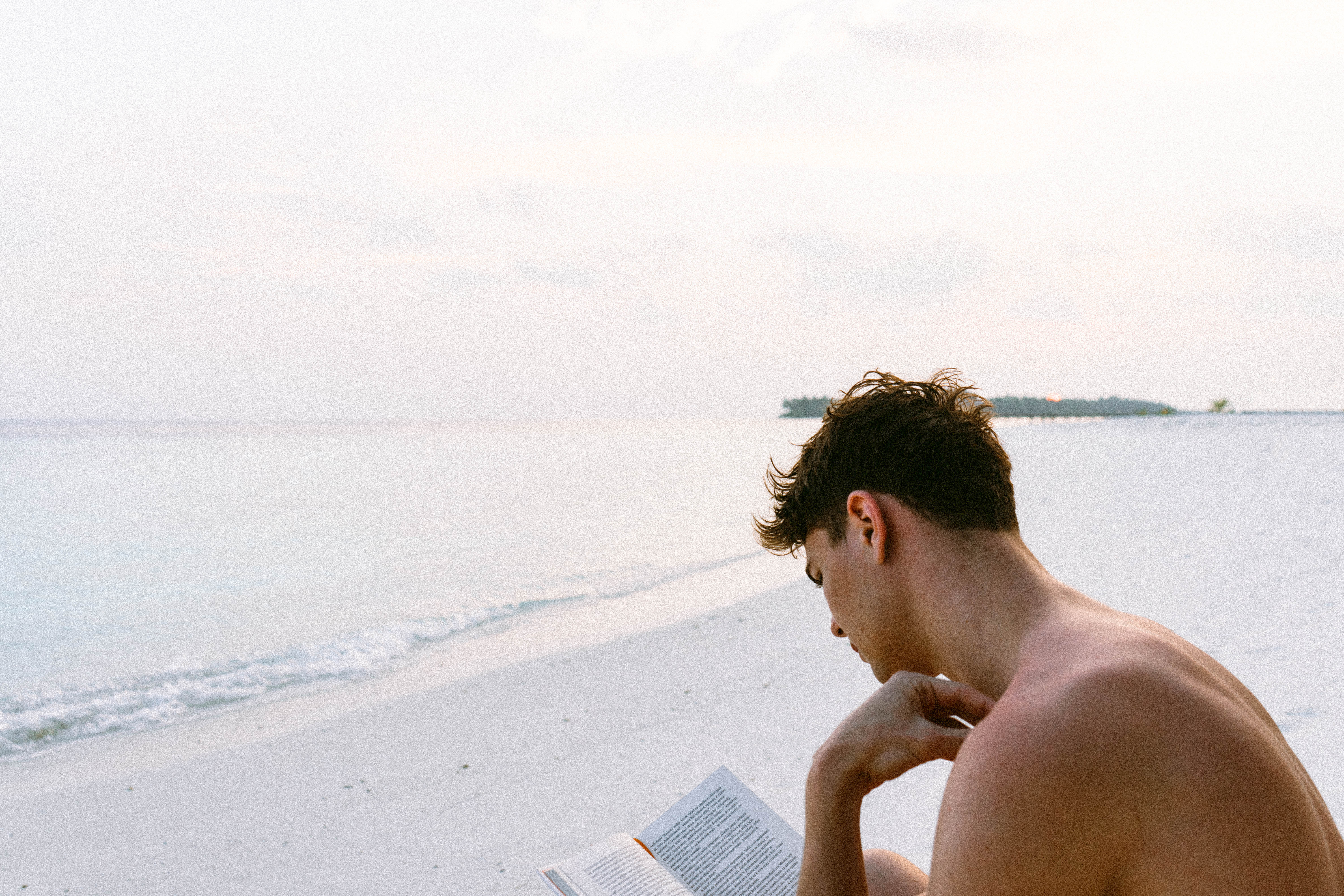 Topless man reading book while seating at beach photo