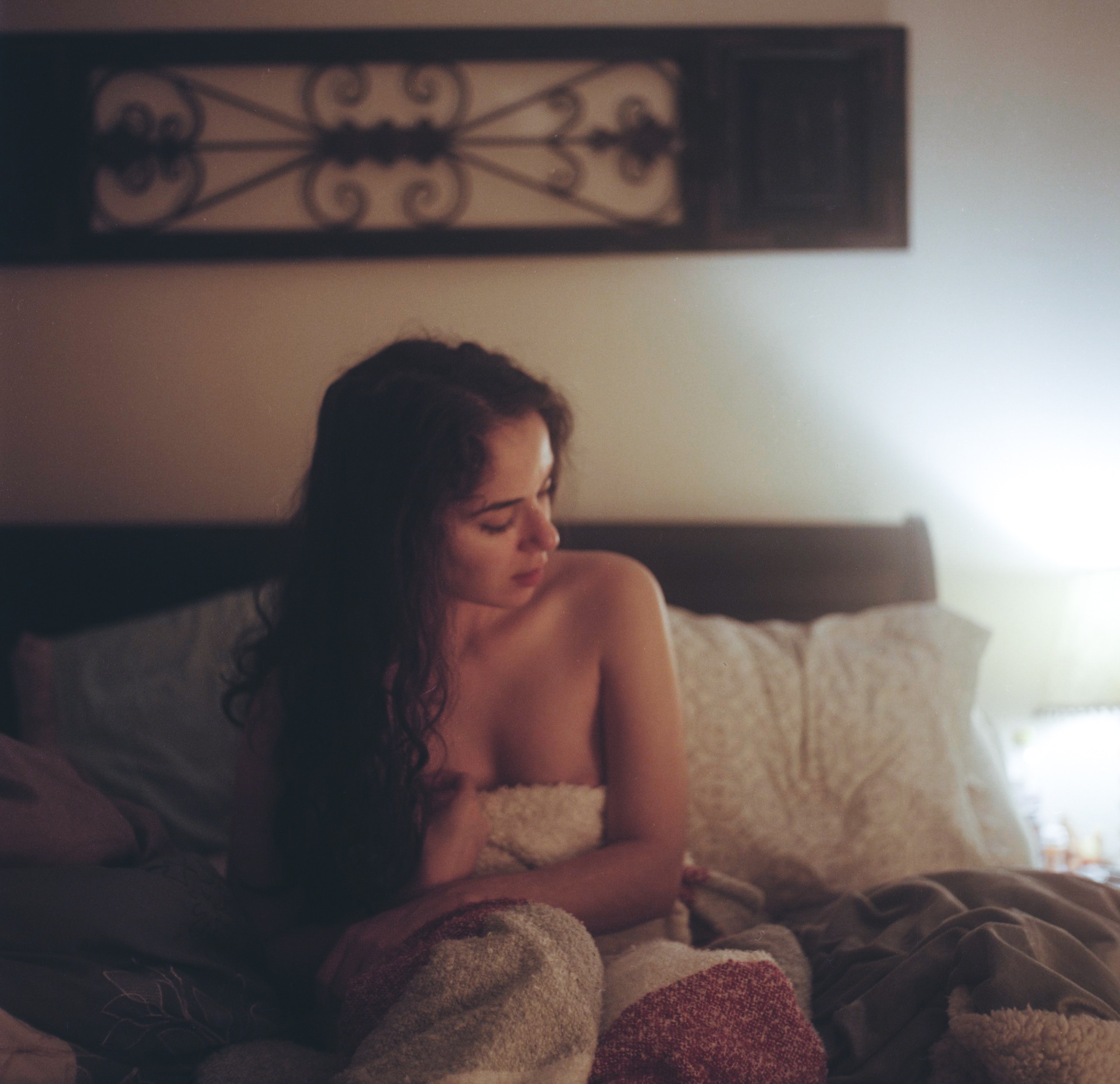 Topless woman with white and red blanket on bed with pillows under brown frame inside white painted room photo