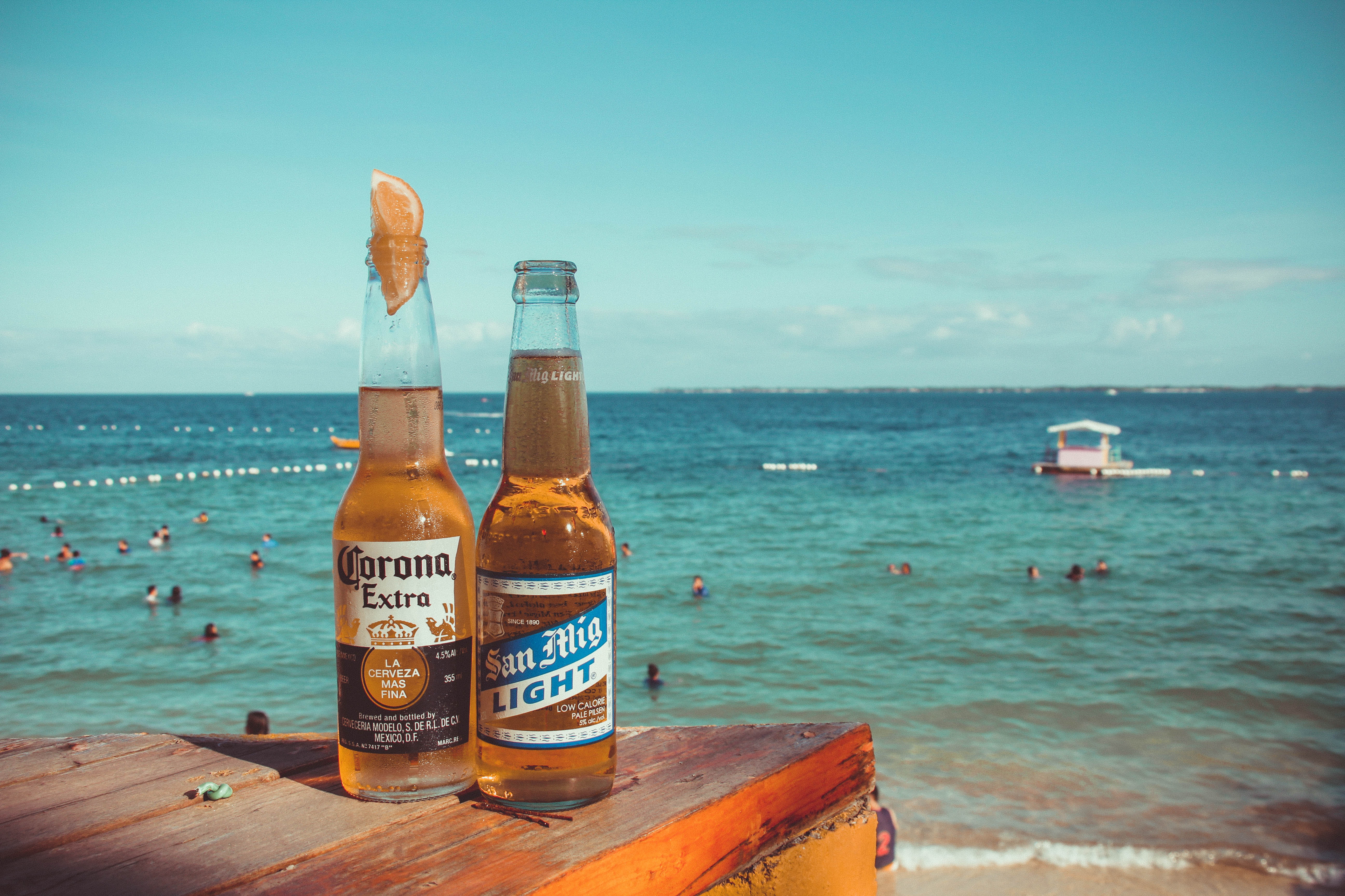 Two corona extra and san mig light beers on top of brown wooden plank near beach photo