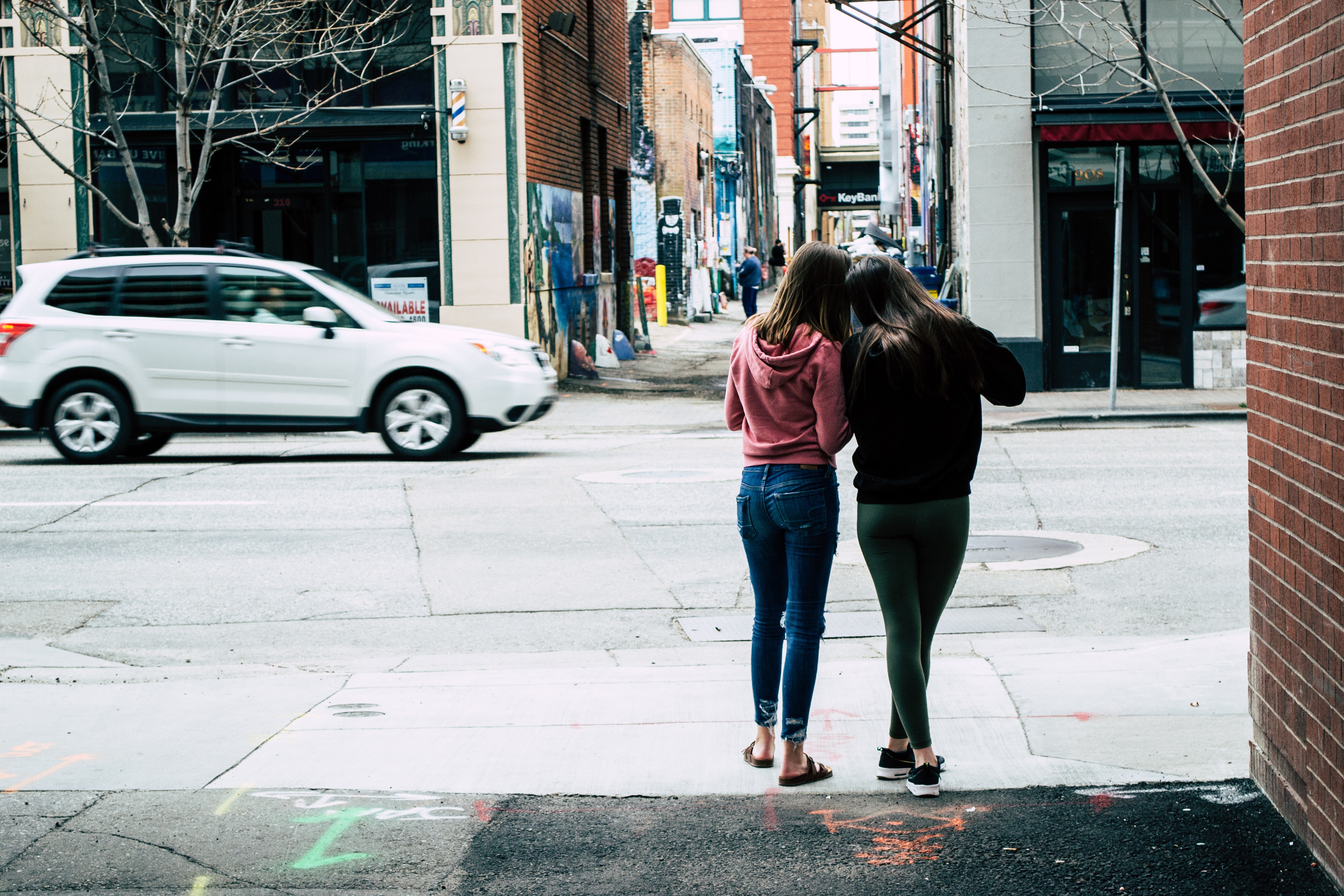 Two girls in jeans show something to each other, standing on the street, Two girls in jeans show something to each other, standing on the street