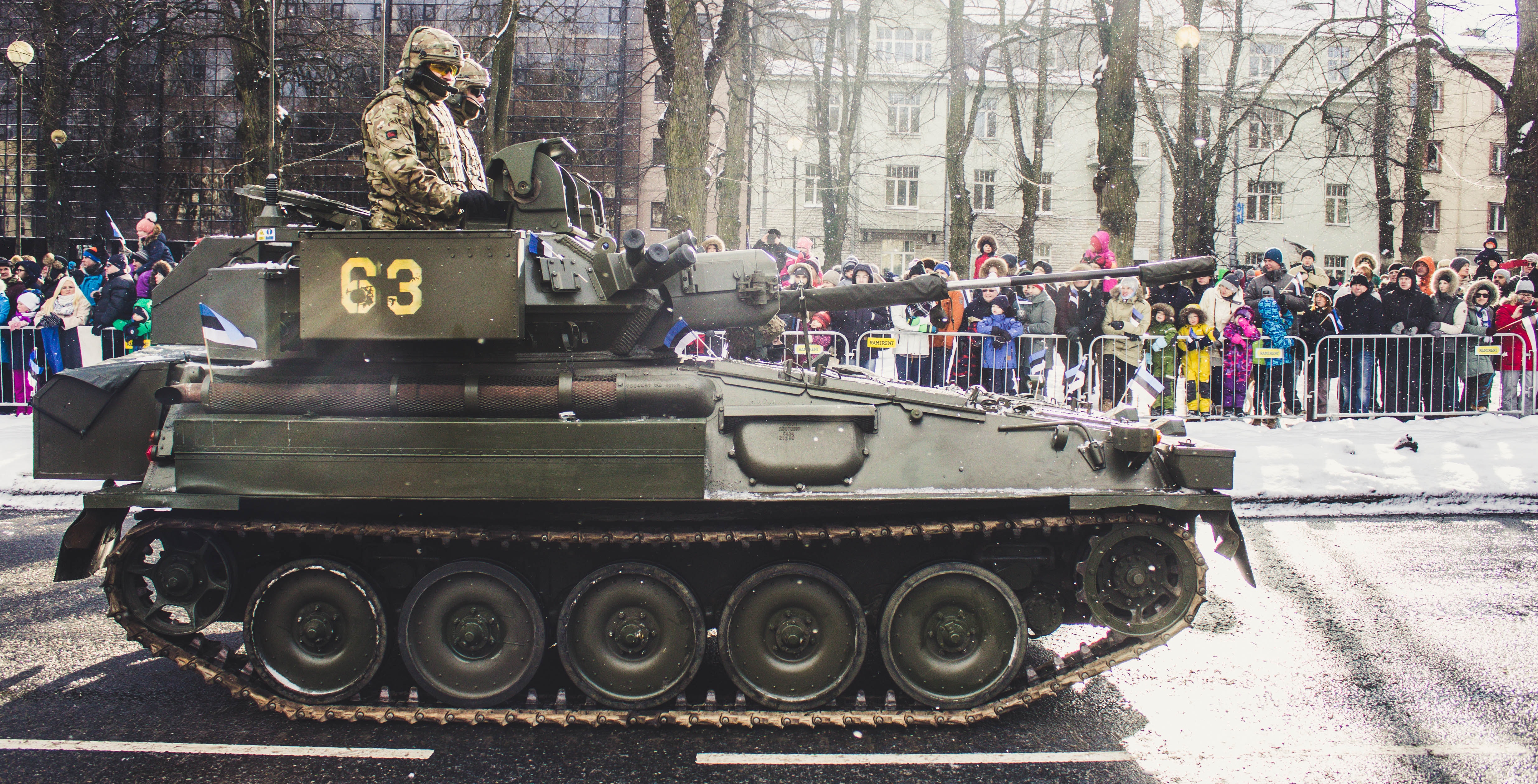 Two soldiers ride on green military tank surrounded with people photo