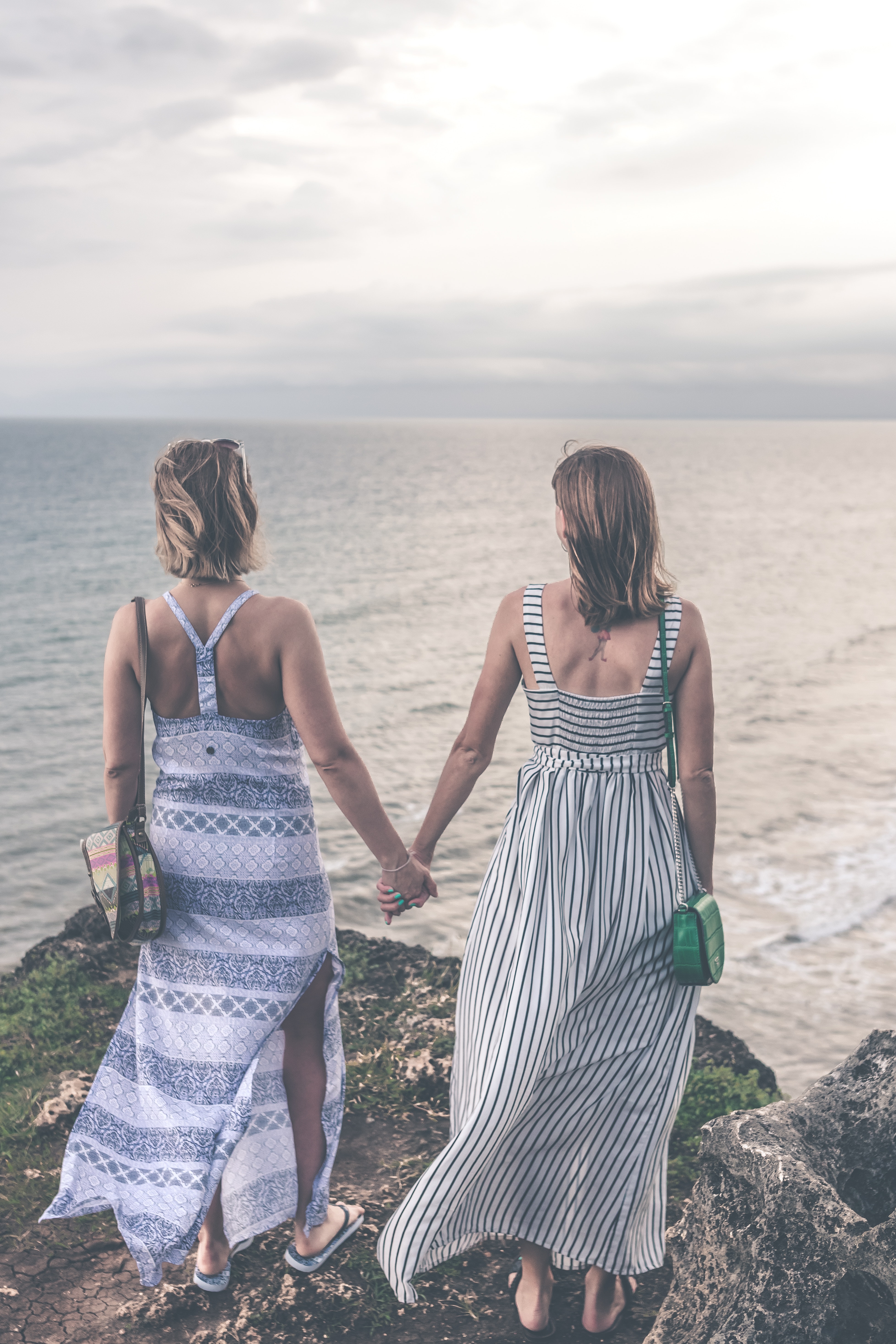 Two women wearing sleeveless dress holding each others hand on cliff photo