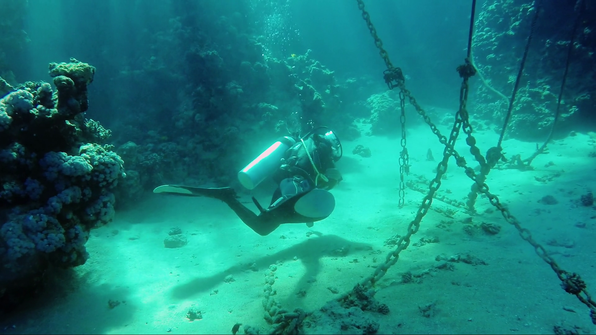 Diver underwater swims near the anchor chains in the sun. A ...