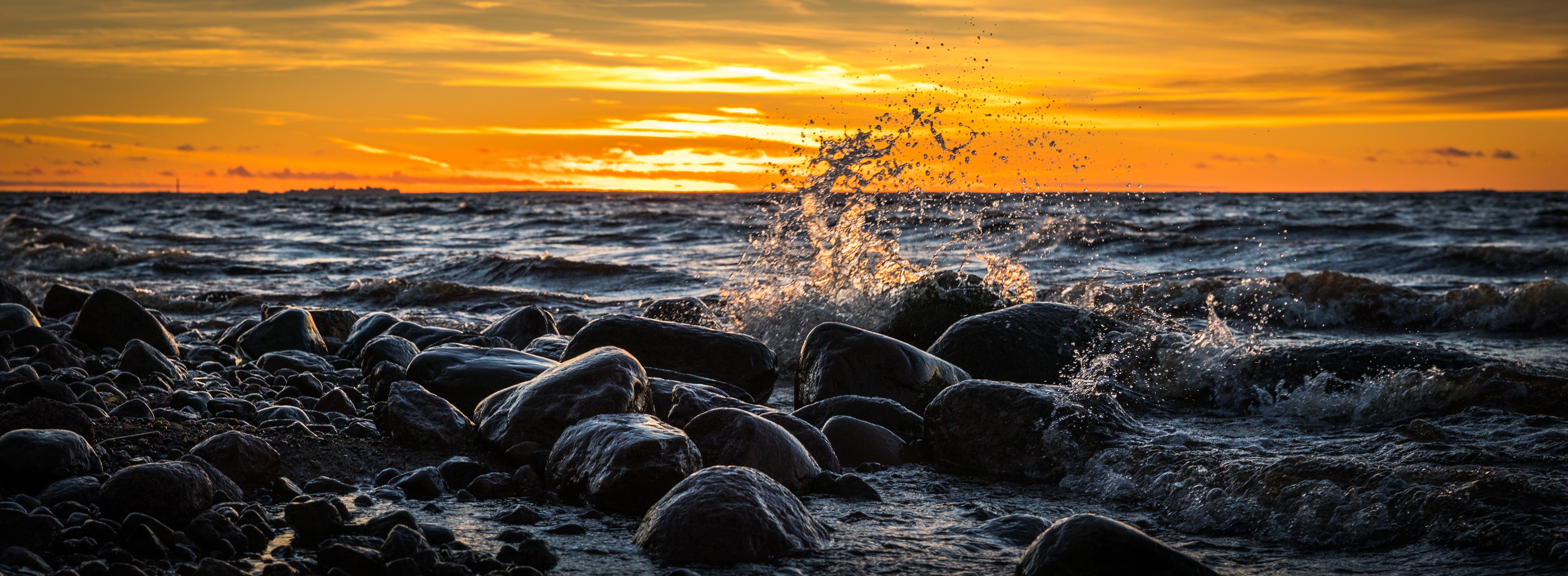 Waves splashing at stones on beach during sunset photo