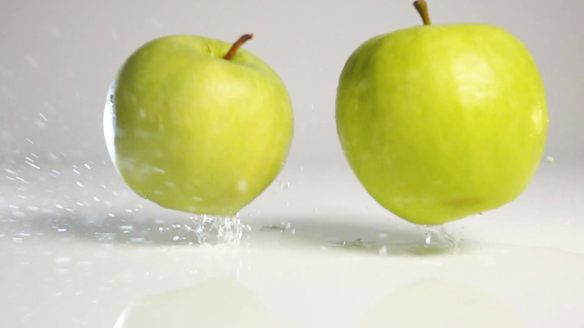 Two fresh green apples falling down and jumping on wet white floor ...