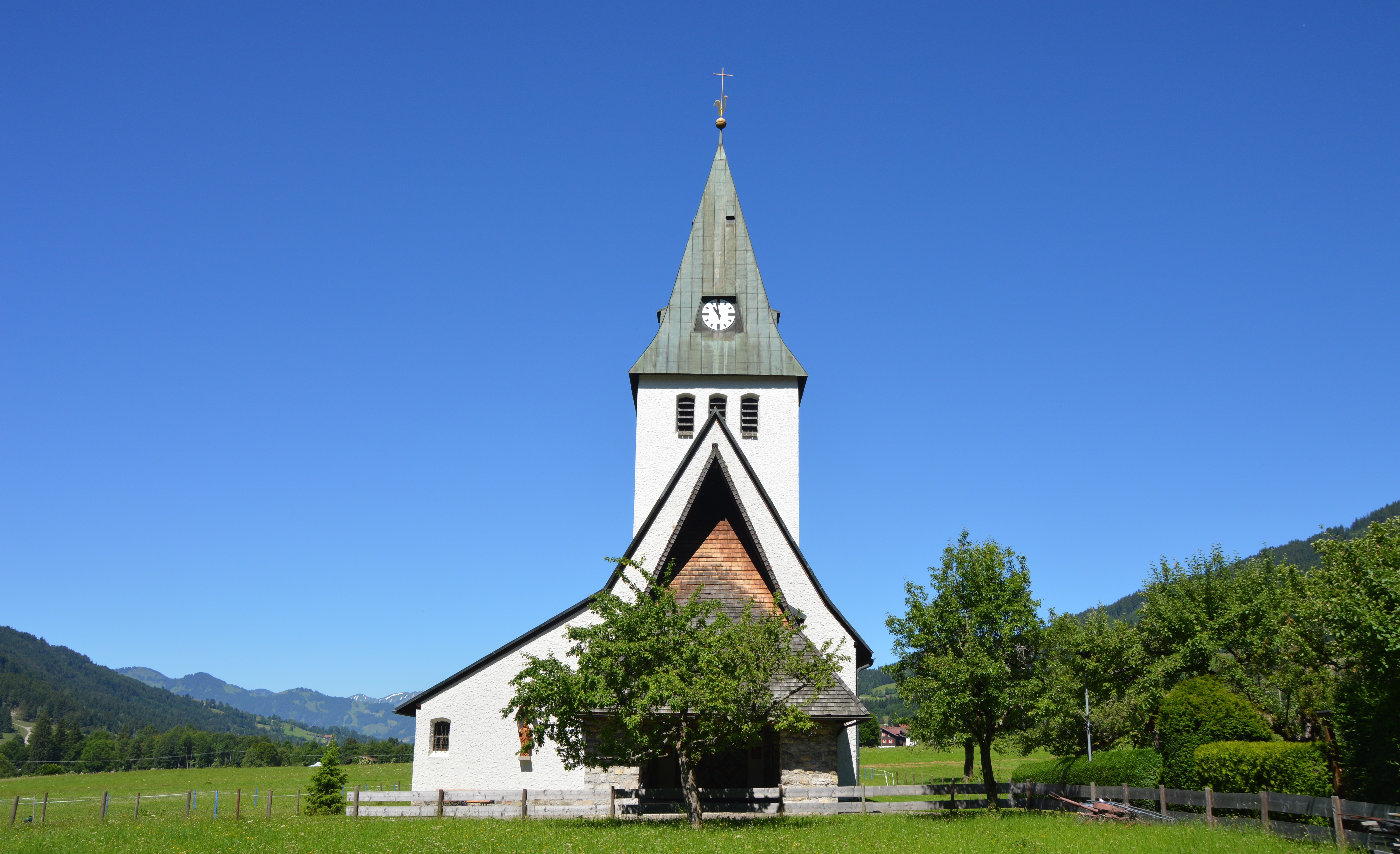 White and grey church near trees under clear blue sky during daylight photo