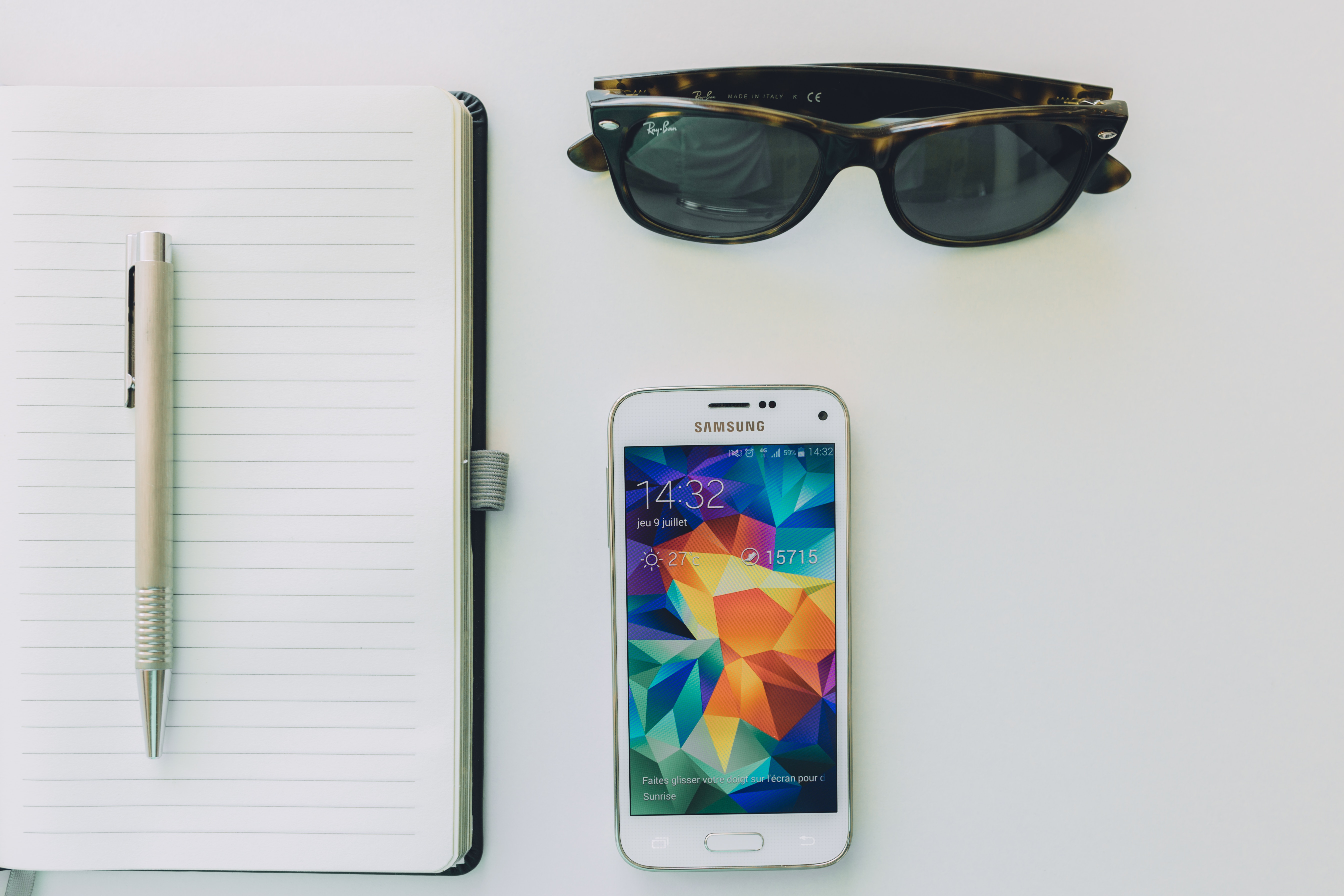 White samsung smartphone beside sunglasses,pen and white notebook photo